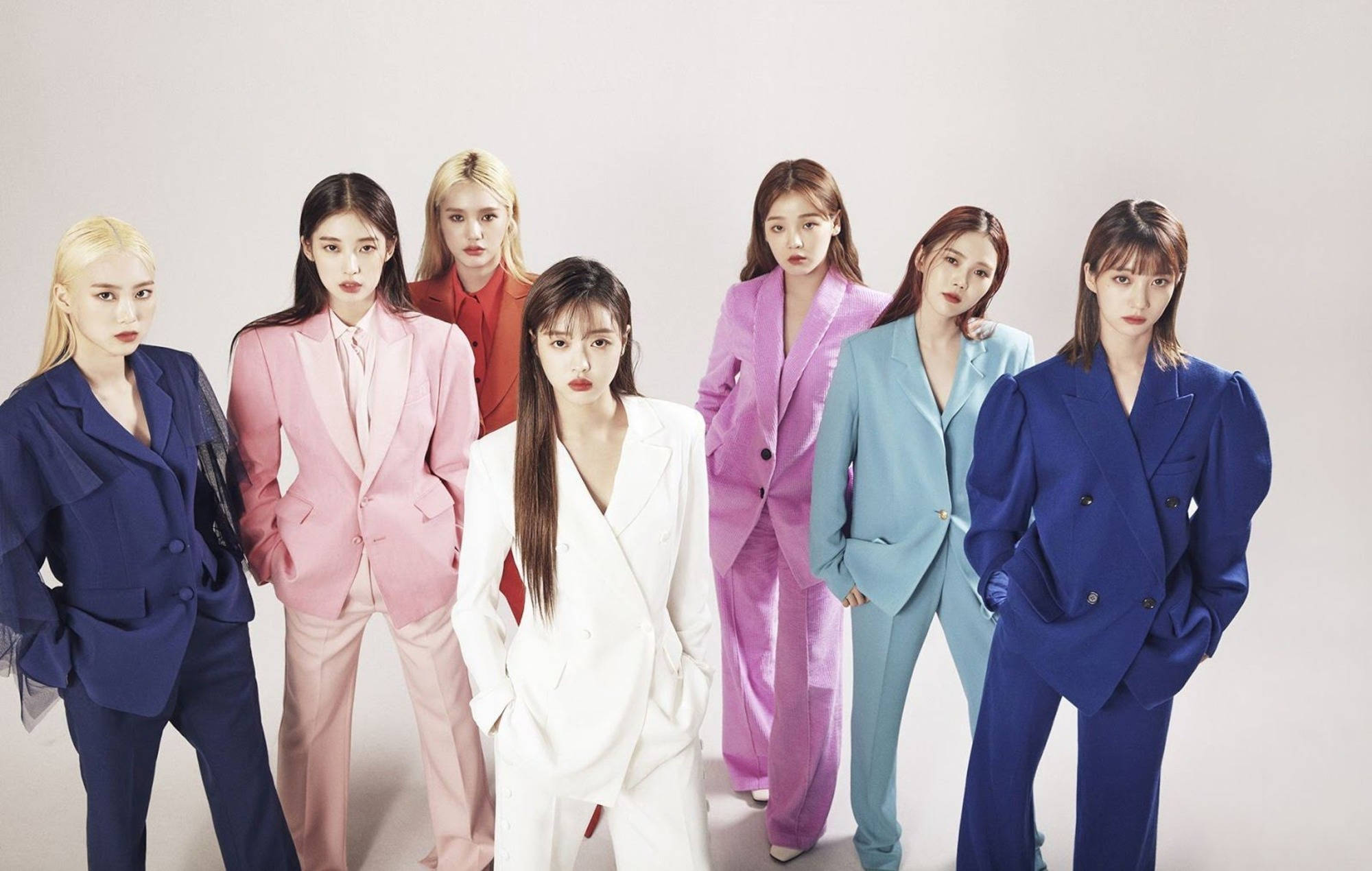 Oh My Girl 色彩繽紛西裝造型 壁紙 — 七位身穿大膽彩色西裝的女性在純白色攝影棚背景前自信地擺姿勢。