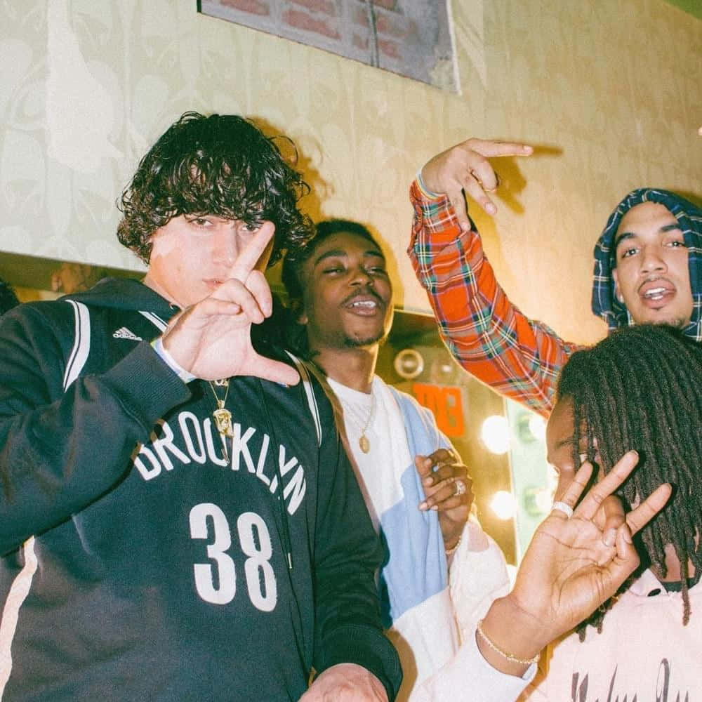 Ohgeesy 與 Shoreline Mafia 壁紙 — 四位年輕男性在溫暖照明的室內環境中擺出和平手勢，穿著休閒街頭服飾和金色首飾。