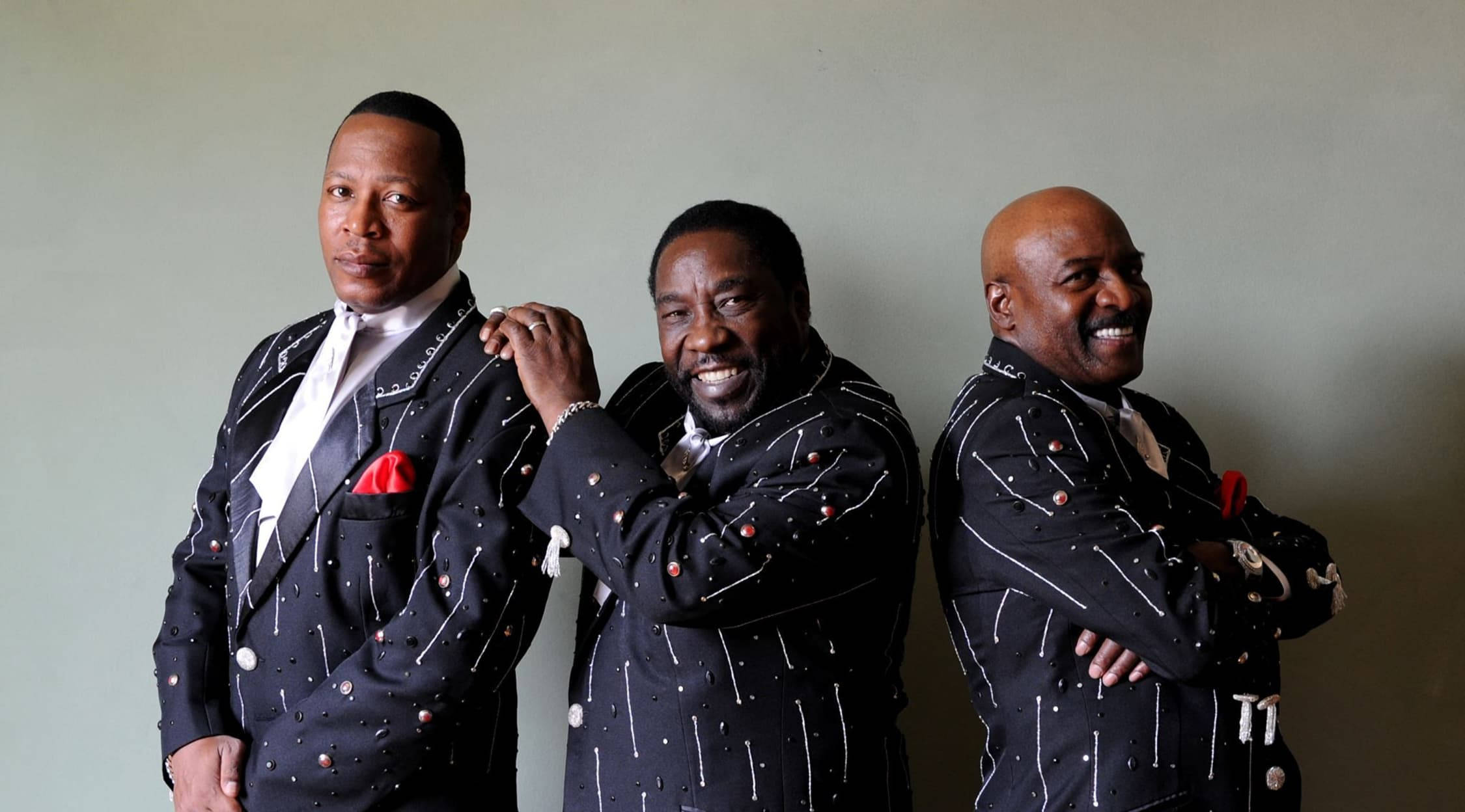Ojays 經典歌曲歌詞播放清單 壁紙 — 三位時尚男士身穿相配的黑色閃片西裝，搭配紅色袋巾，自信地靠在素牆上擺姿勢。