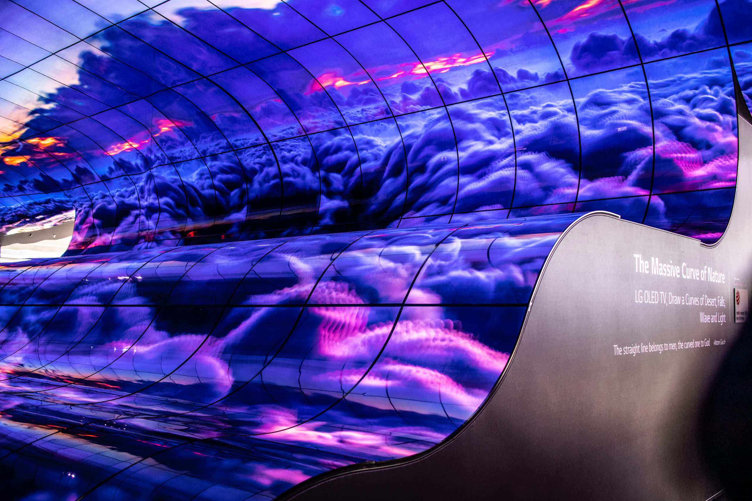 OLED 雲彩圖 壁紙 — 彎曲的OLED電視顯示屏展示了一個充滿活力的紫色和粉紅色雲彩天空，日落色調反射在其光滑表面上。