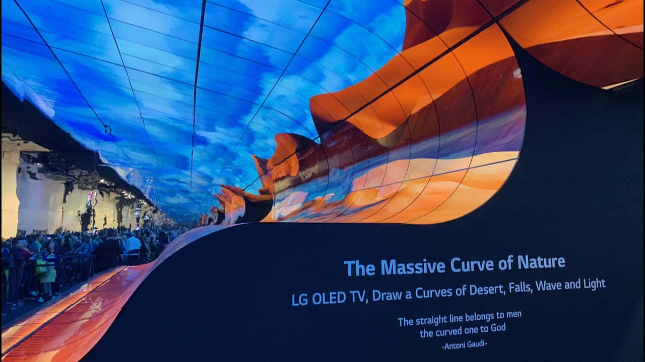 OLED 電視沙漠圖 壁紙 — 彎曲的LG OLED電視顯示屏展示了一個充滿活力的沙漠峽谷，藍天白雲下，人群在下方觀看。