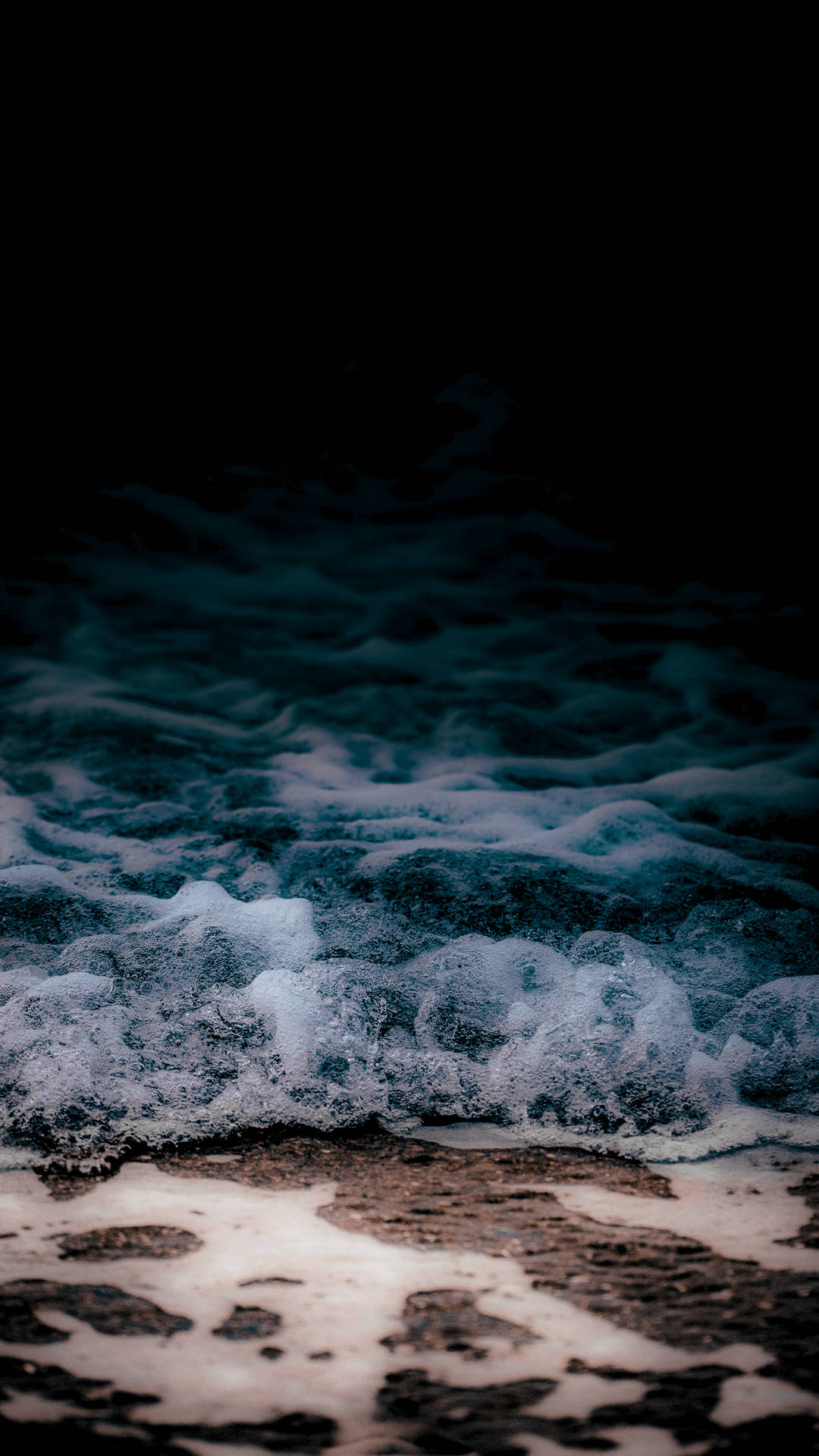 夜間泡沫海浪拍打黑暗的海灘。