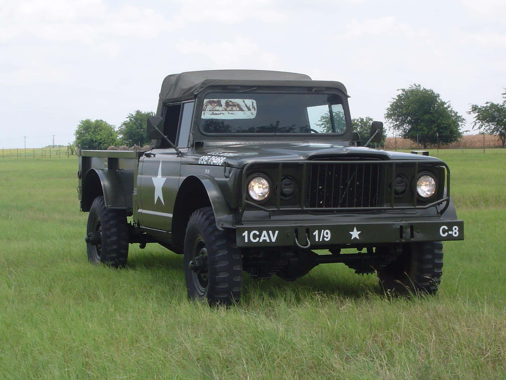 Jeep Gladiator 桌布 壁紙 — 一輛帶有白色星星標記的堅固橄欖綠色軍用吉普車停放在高草叢生的田野中，天空多雲。