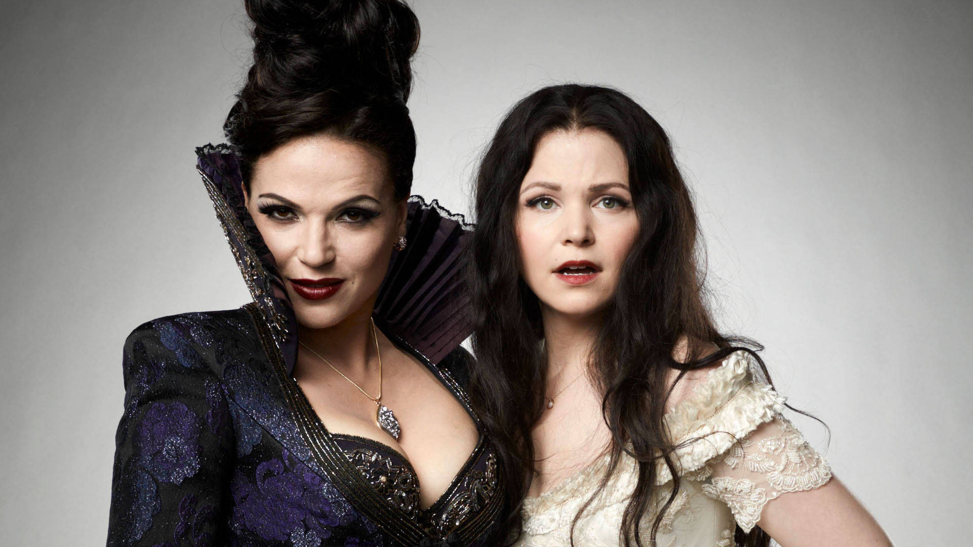 《Once Upon A Time》魔法森林中的親密家族 壁紙 — 兩位身穿對比鮮明深淺色復古服裝的女性，在純灰色背景前擺出姿勢，表情強烈。