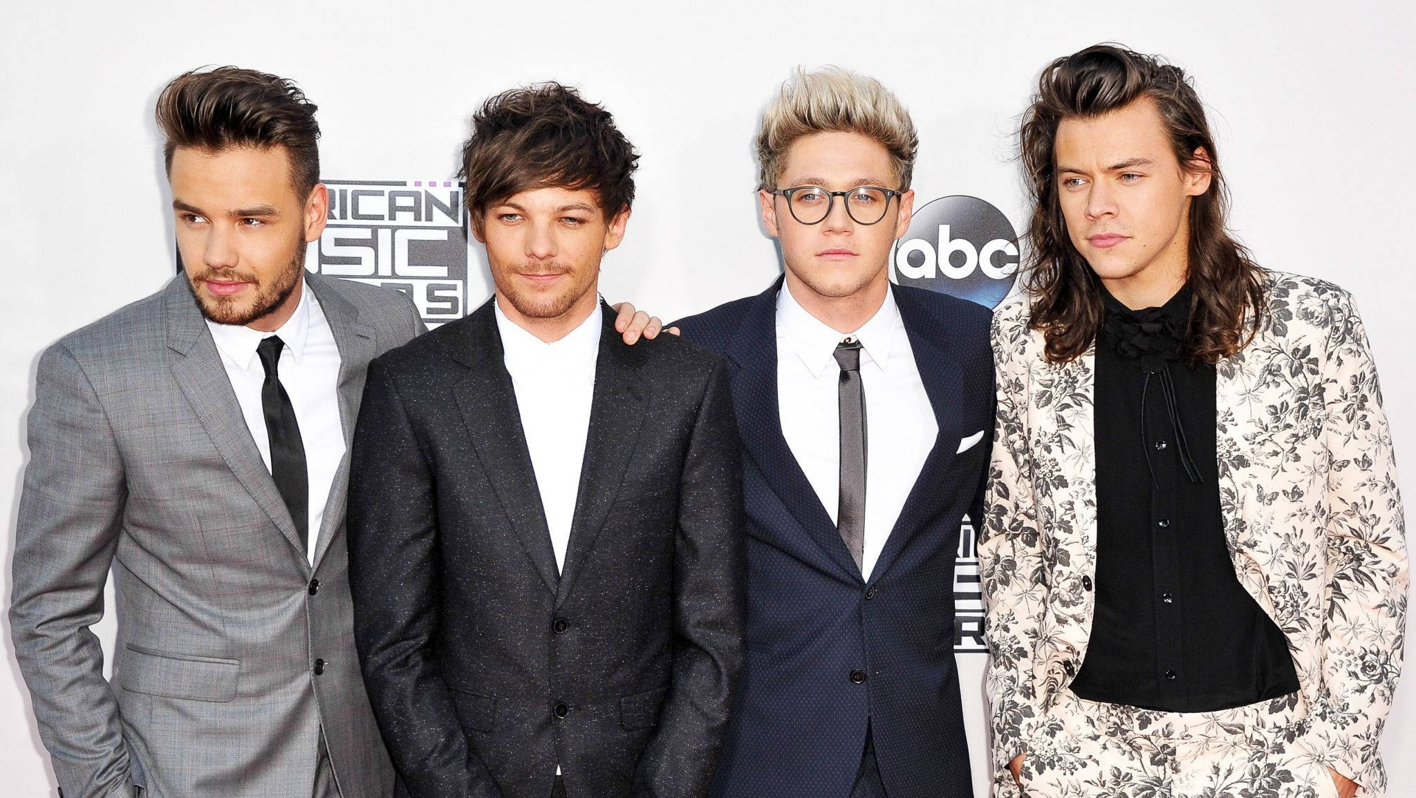 One Direction 紅毯風采 壁紙 — 四位穿著正式西裝的時尚男士在音樂頒獎典禮上自信地擺姿勢，背景帶有品牌標誌。