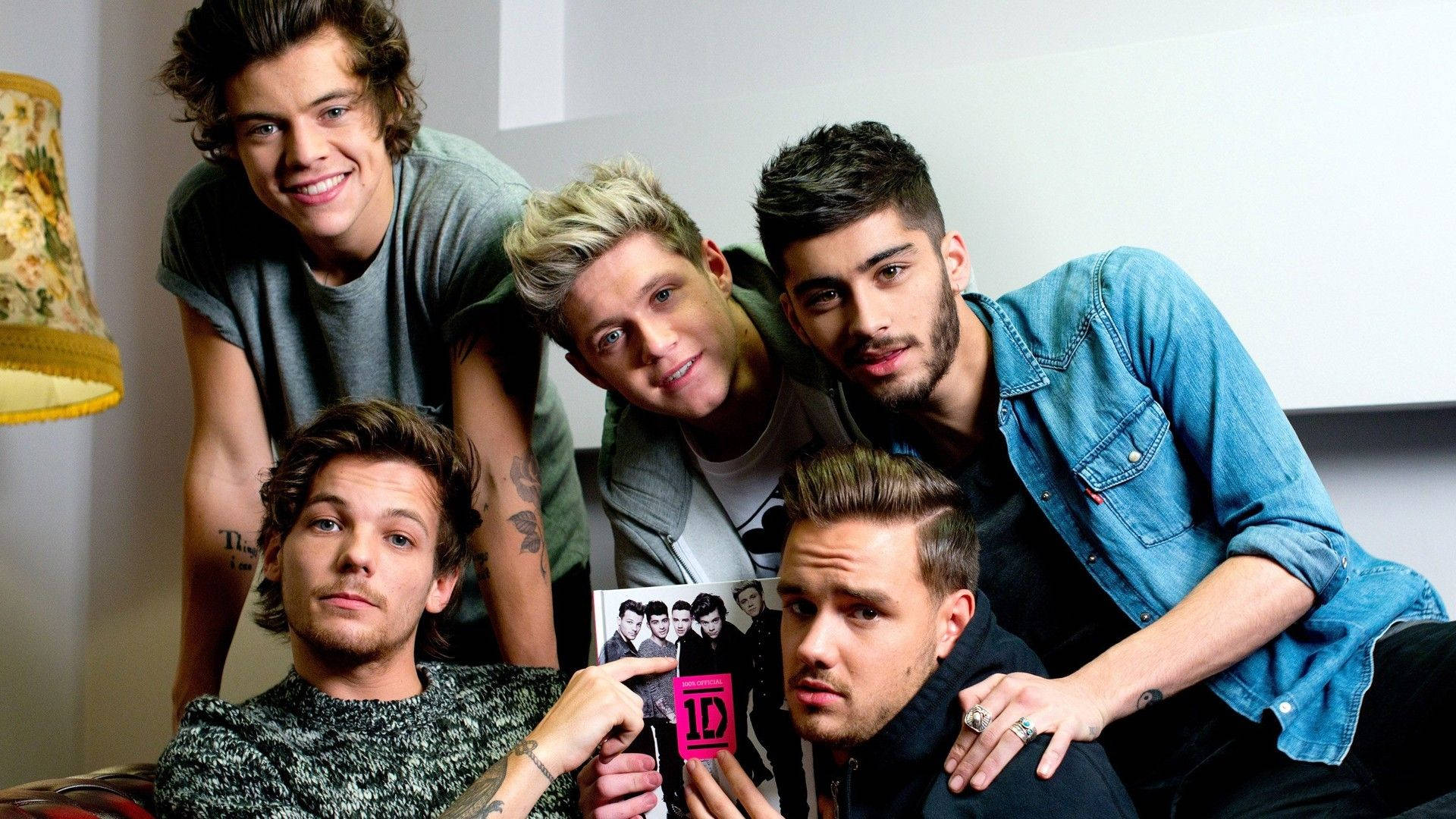 「One Direction登上雜誌封面！」 壁紙 — 五位身穿休閒服的年輕男子在室內緊密地擺姿勢，微笑著並拿著自己的照片。