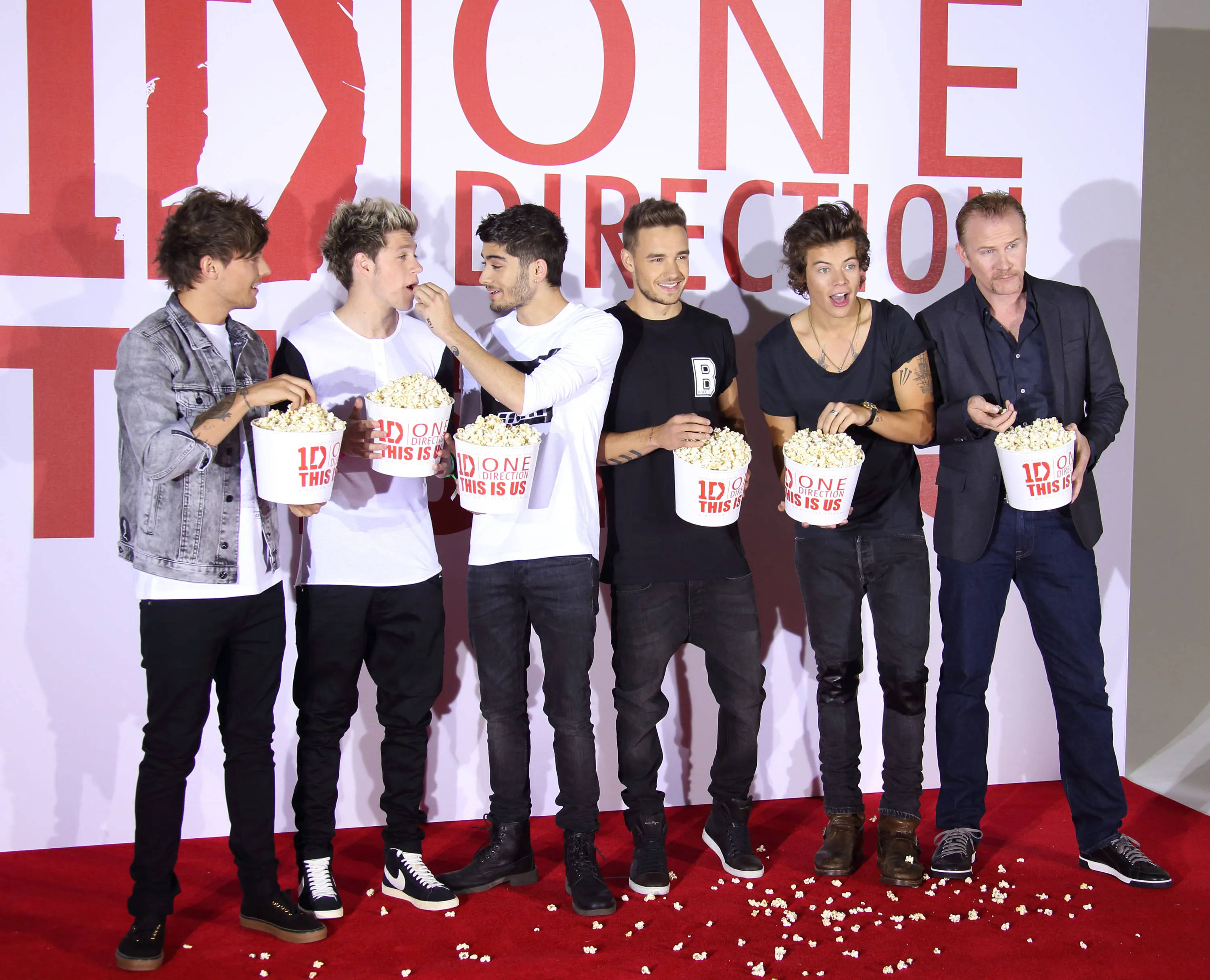 One Direction Aesthetic 桌布 壁紙 — One Direction 樂隊成員在大型「1D」背景前的紅地毯上大笑並分享爆谷。