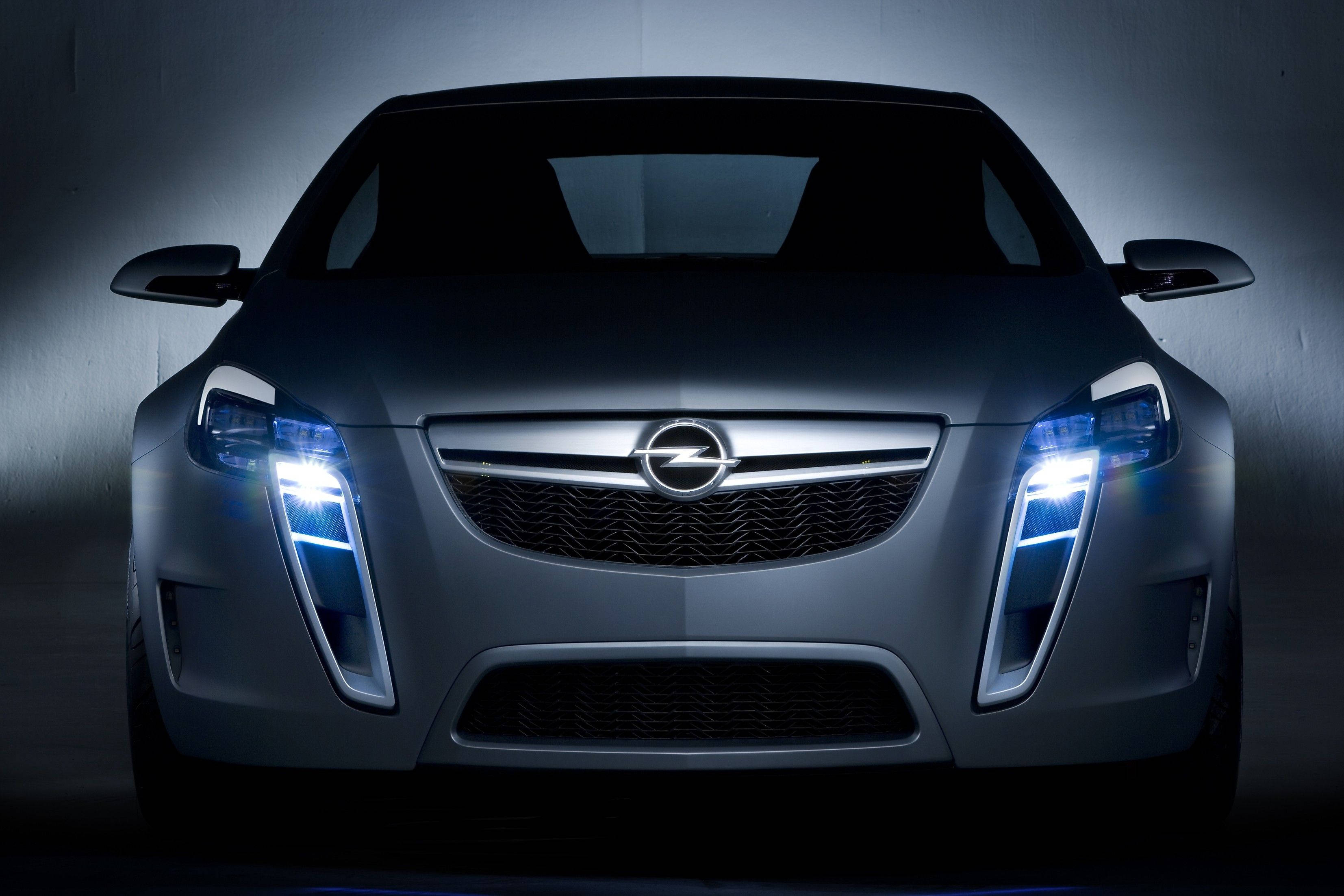 灰色奧派（Opel）前視圖 壁紙 — 一輛時尚的銀色歐寶概念車，帶有發光的藍色頭燈，在黑暗的攝影棚環境中向前凝視。