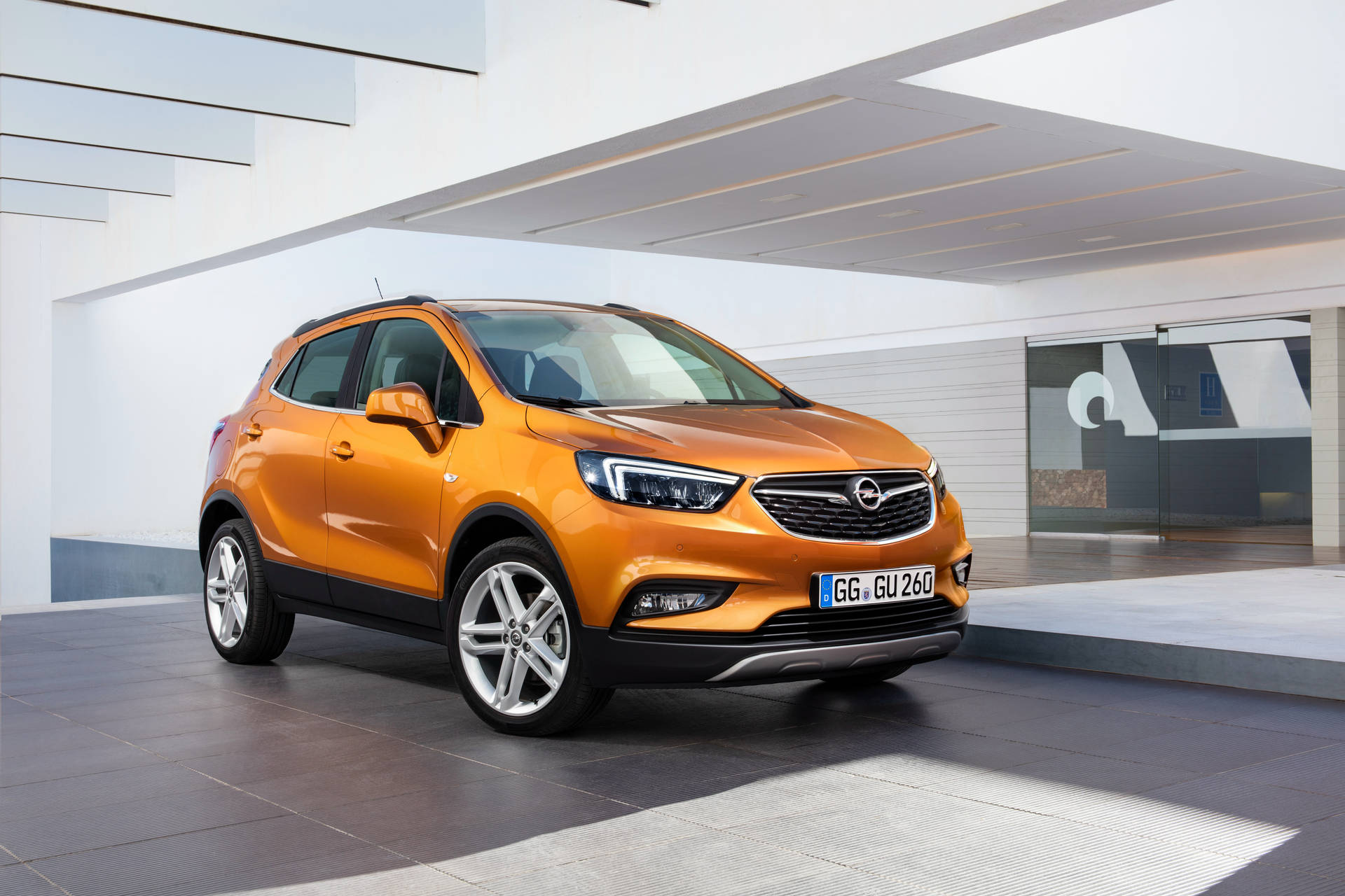 橙色Opel Mokka SUV停放在現代建築空間，玻璃牆壁，線條簡潔。