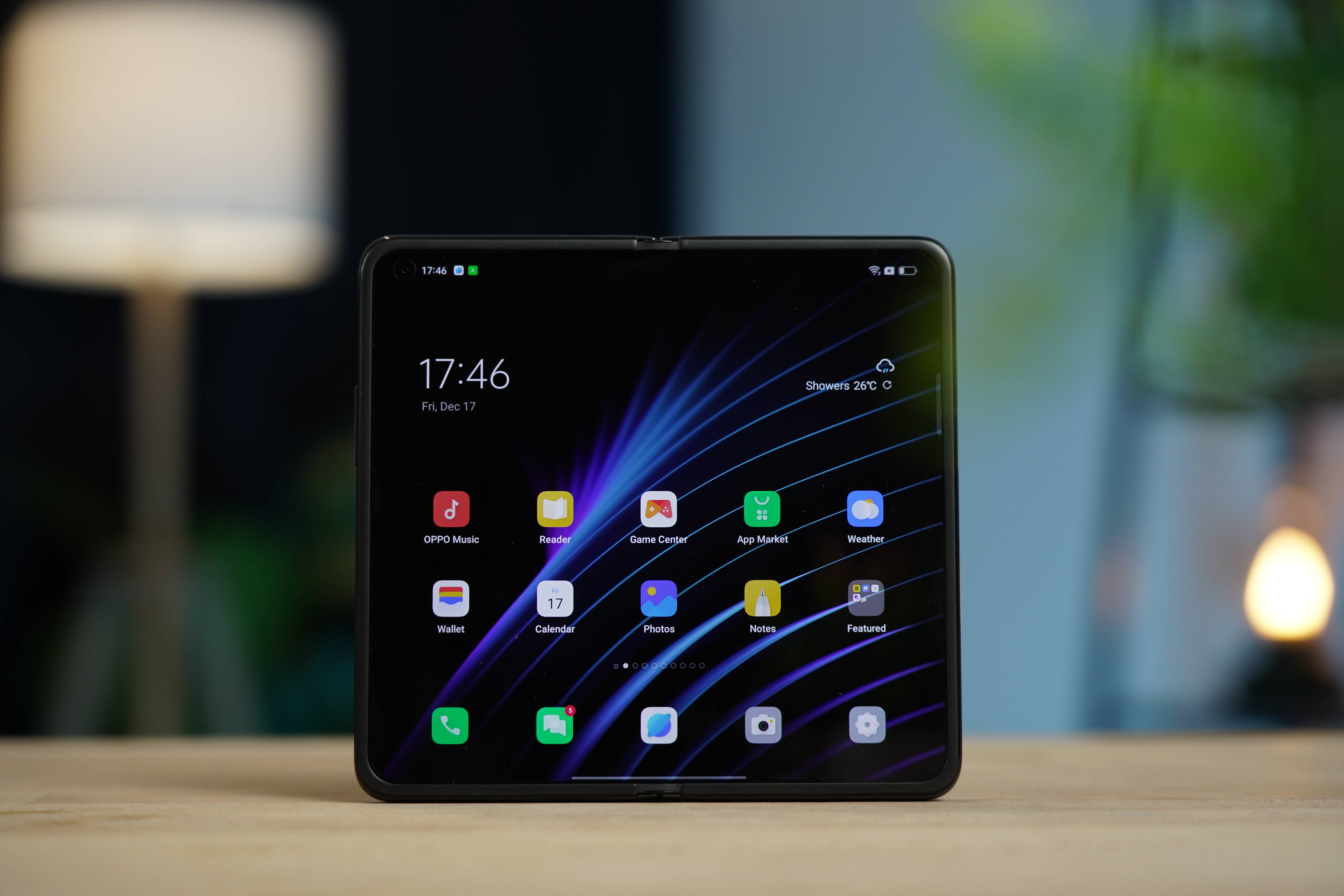Oppo Find N 可摺疊智能手機 壁紙 — 一部時尚的黑色摺疊智能手機在木桌上顯示充滿活力的應用程式網格，背景是動態的紫藍色光條壁紙，帶有柔和模糊的背景燈光。