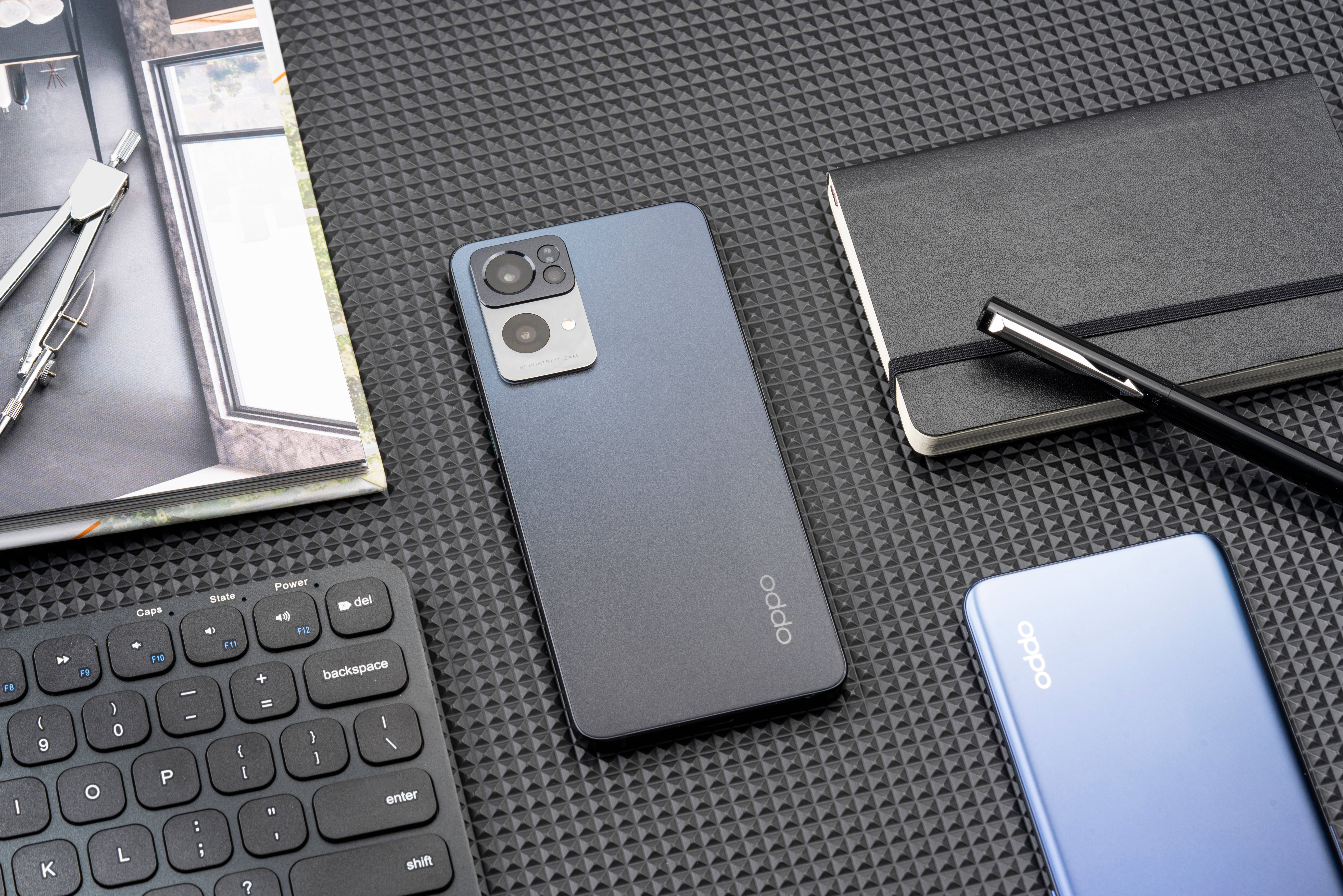 與 Oppo 共度工作日 壁紙 — 兩部OPPO智能手機放在一張有紋理的黑色桌子上，旁邊有鍵盤、筆記本和指南針。