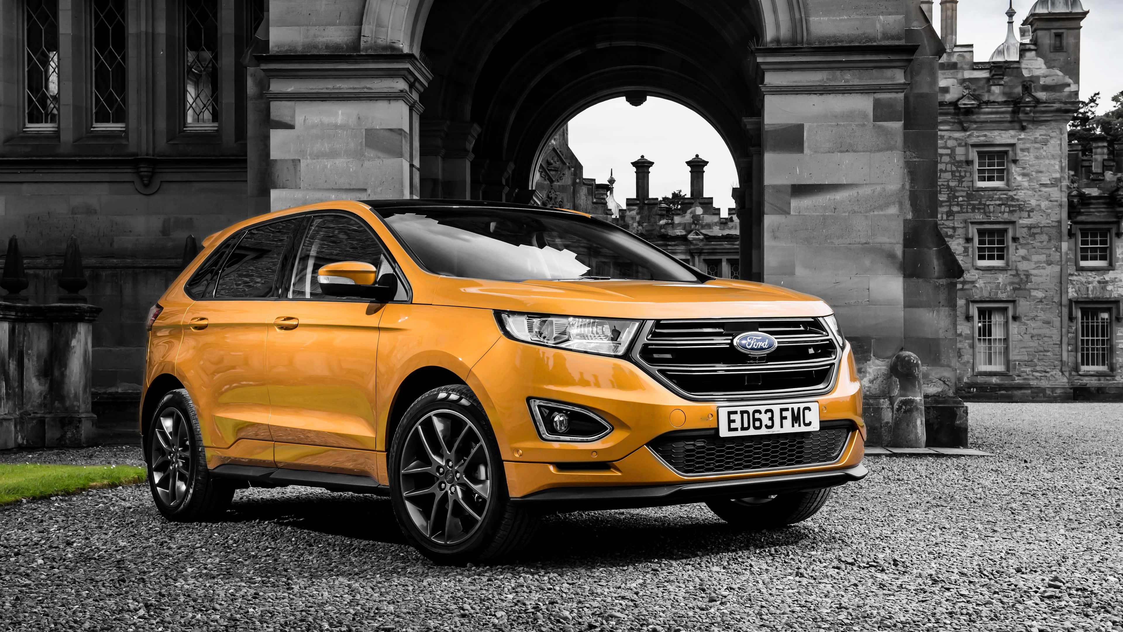 Ford Edge 桌布 壁紙 — 一輛充滿活力的橙色福特Edge SUV在單色歷史石拱門和城堡式建築背景下脫穎而出。