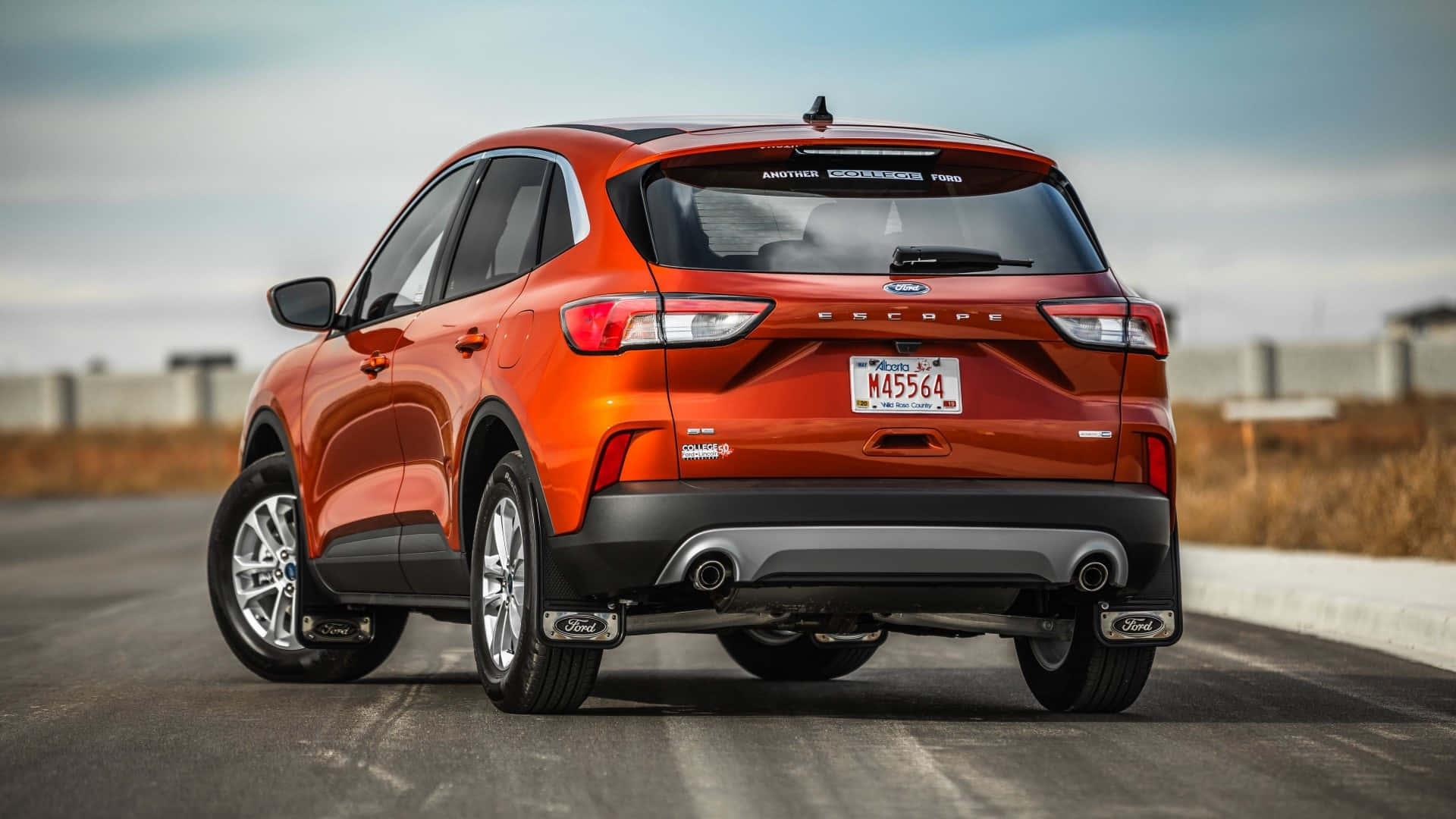 Ford Escape 桌布 壁紙 — 一輛鮮橙色的福特 Escape SUV 從後方觀看，在陰天下行駛在鋪砌道路上。