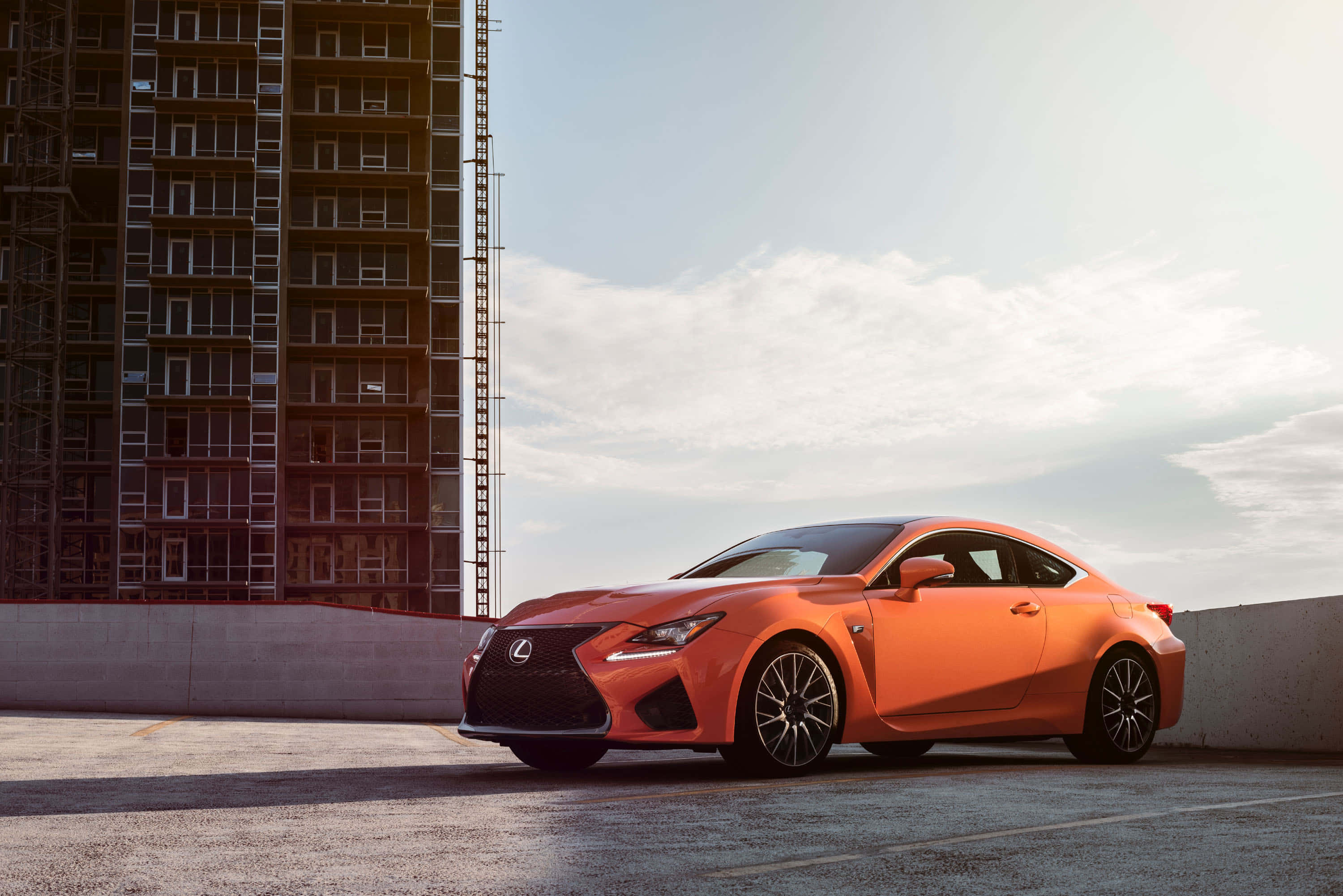 Lexus Rc F 桌布 壁紙 — 一輛鮮豔的橙色Lexus跑車停泊在混凝土天台，旁邊是一座正在興建的高樓，天空晴朗。