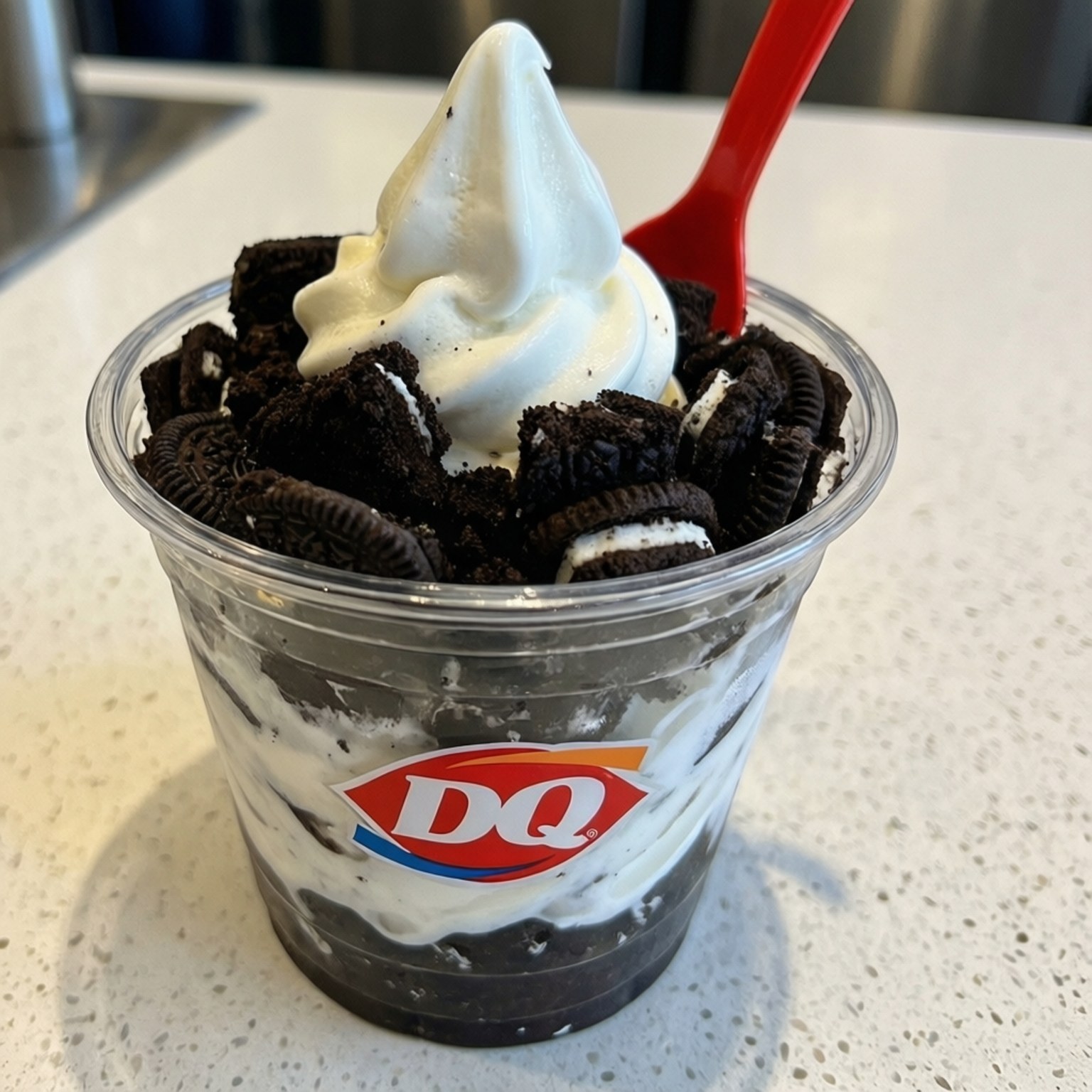 Oreo Blizzard分層 壁紙 — 透明杯裝DQ Oreo軟雪糕，上面有壓碎嘅曲奇餅同紅色匙羹，放喺有斑點嘅枱面上。
