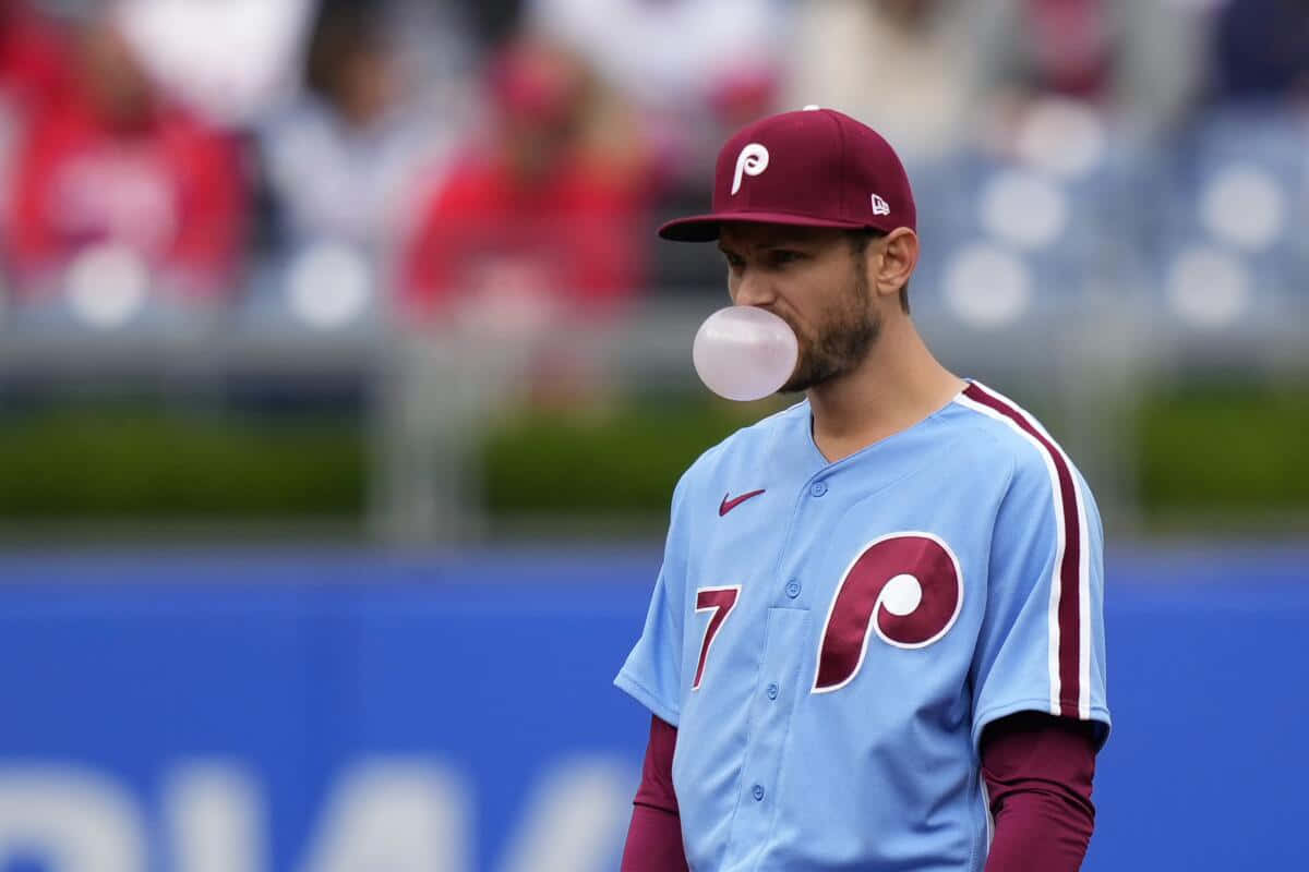 Trea Turner Phillies 桌布 壁紙 — 一名身穿淺藍色和栗色制服嘅棒球手喺球場上吹緊一個大泡泡糖波波。
