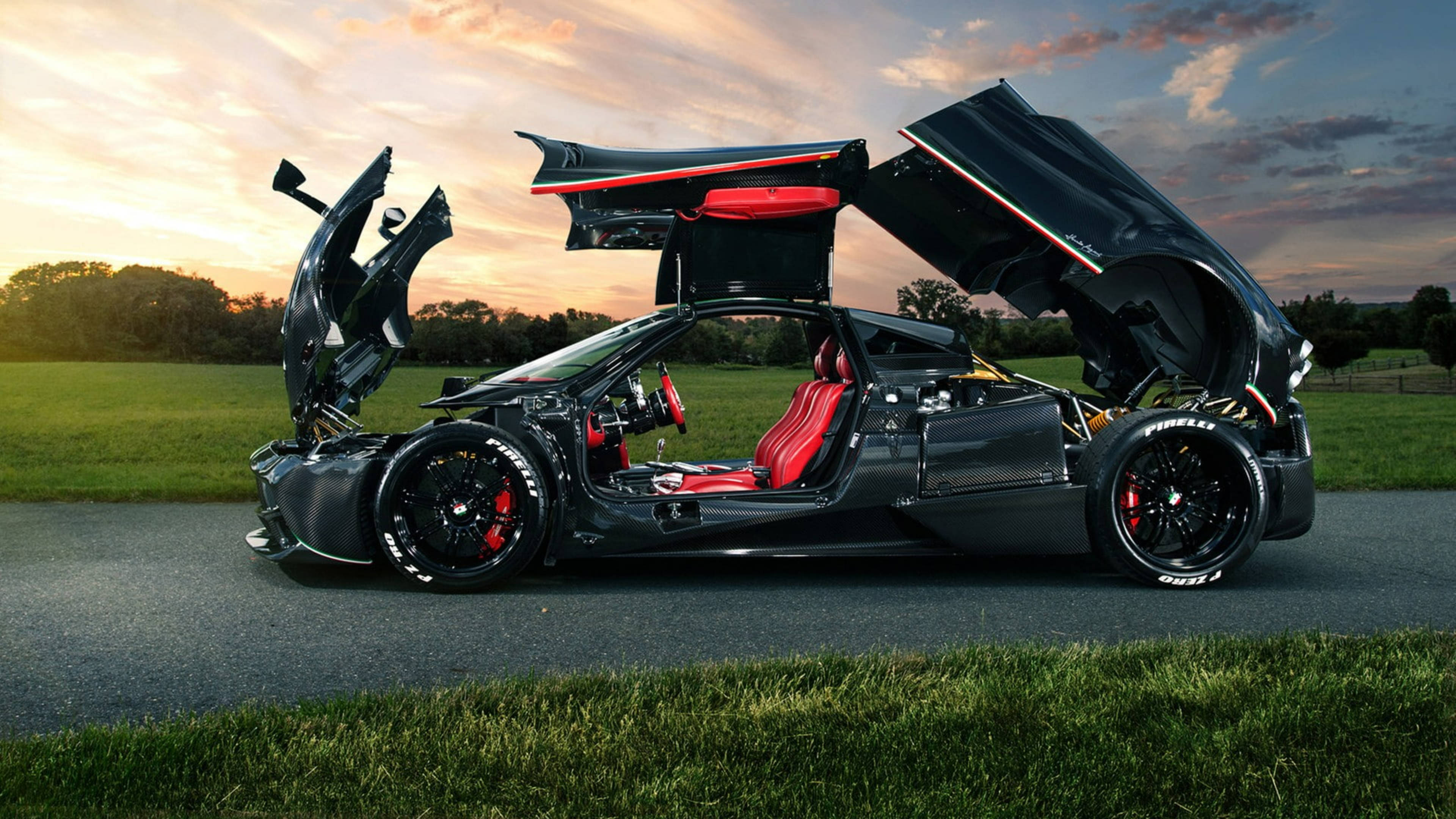 Pagani Huayra La Monza Lisa 特別版 壁紙 — 一輛黑色超級跑車，紅色內飾，蝴蝶門打開，停在日落時分的道路上，後面是草地。