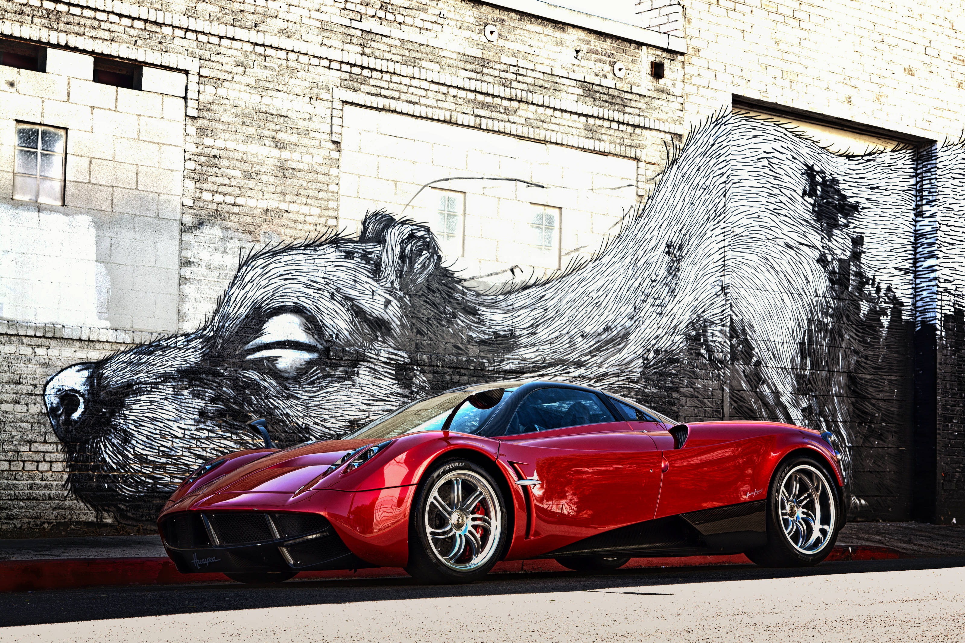 Pagani Huayra 紅色款搭配塗鴉藝術 壁紙 — 一架亮紅色跑車停泊在磚牆上巨大的黑白睡狼壁畫前。