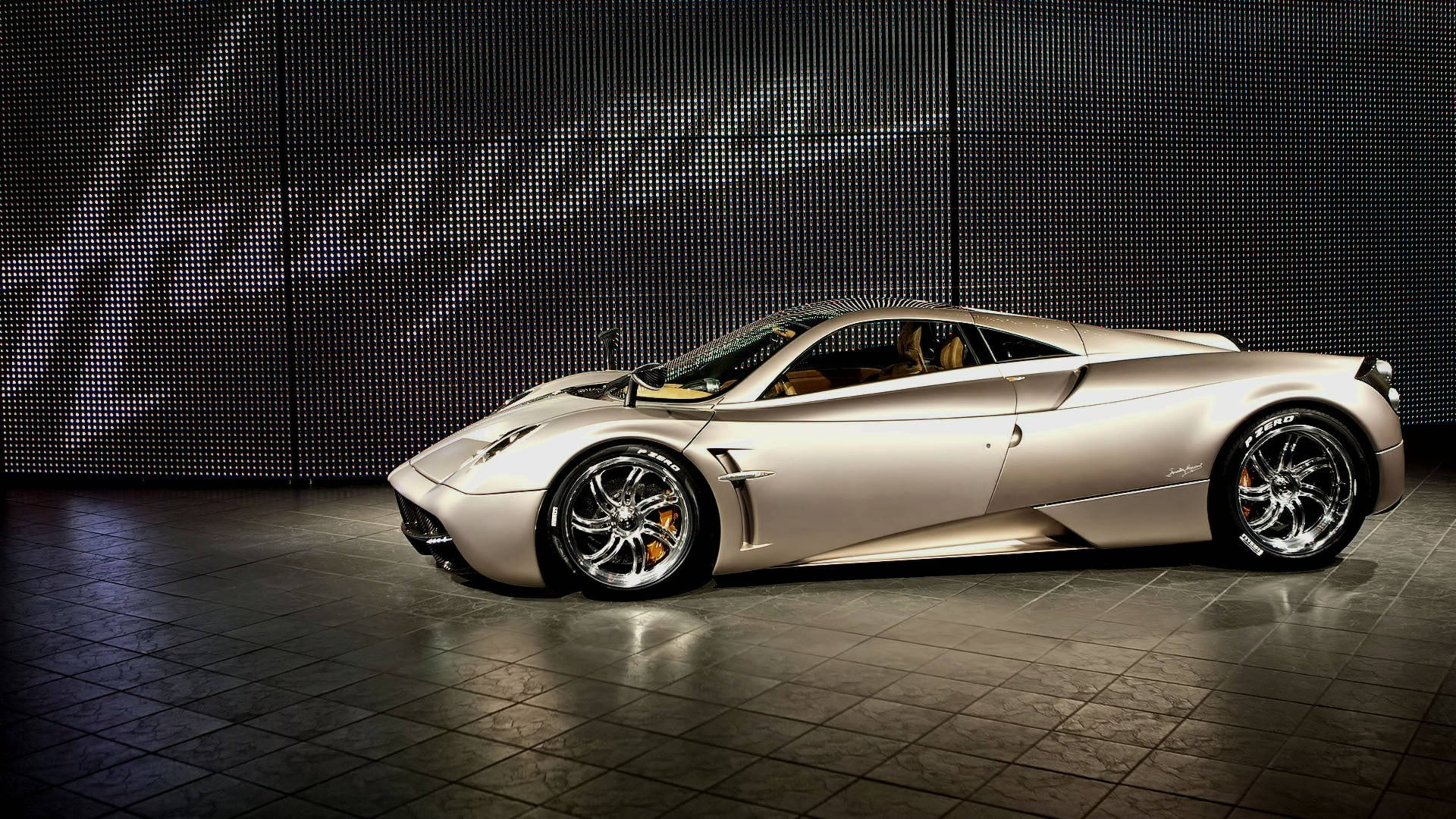 Pagani Huayra 銀色跑車 壁紙 — 一輛時尚的銀色跑車配備發光橙色制動卡鉗，在瓷磚地板上展示，背景為深色像素牆。