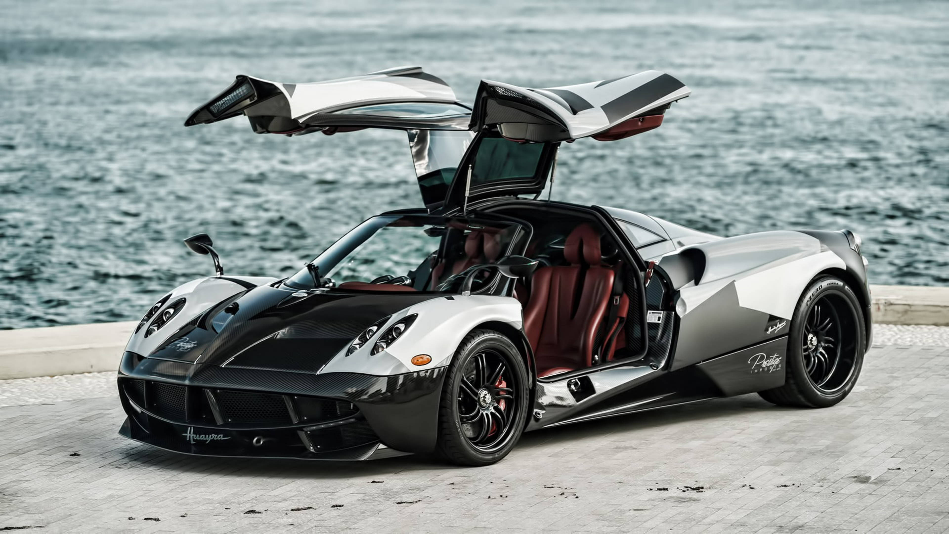 Pagani Huayra 鳥翼門敞開 壁紙 — 一架銀黑配色的Pagani Huayra跑車，剪刀門打開，停在海濱碼頭上，俯瞰海洋。