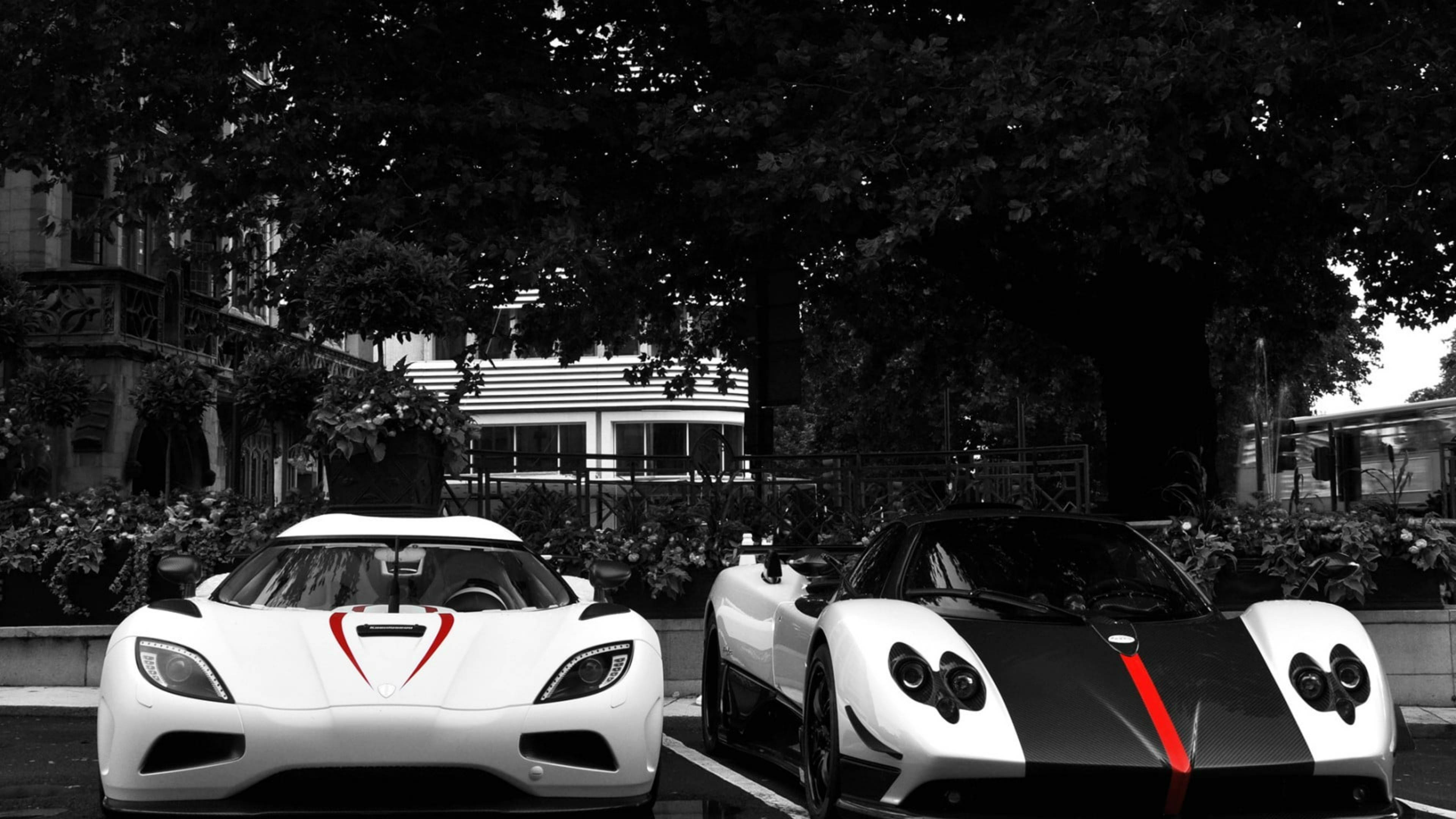 Pagani Zonda Cinque 與 Koenigsegg Agera 壁紙 — 兩輛時尚的白色超級跑車帶有紅色點綴，停放在綠樹成蔭的單色城市環境中。