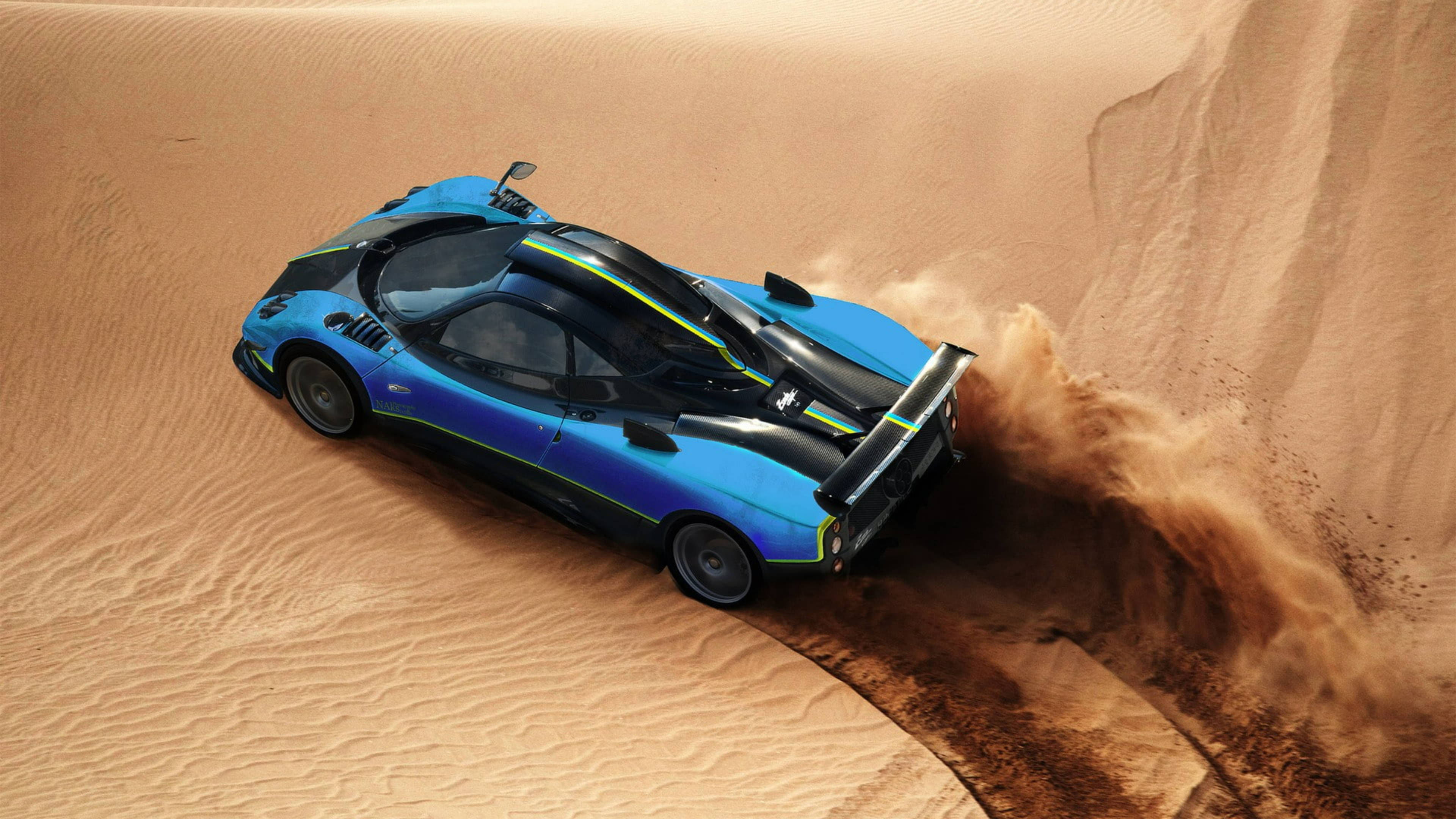 Pagani Zonda Cinque Roadster 沙漠空中視角 壁紙 — 一輛充滿活力的藍色跑車在金色沙漠沙丘中飛馳，揚起沙塵，動態俯拍。
