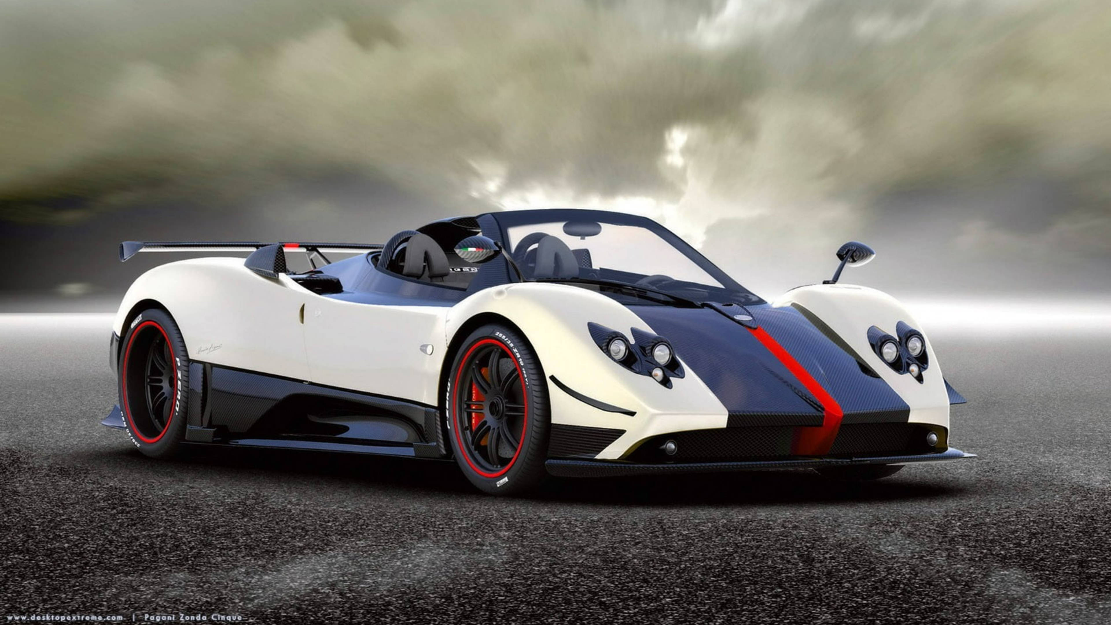 Pagani Zonda Cinque Roadster 壁紙 — 一輛白色和黑色的帕加尼Zonda Cinque敞篷跑車，帶有紅色點綴，在戲劇性的暴風雨天空下，停在潮濕的瀝青路面上。
