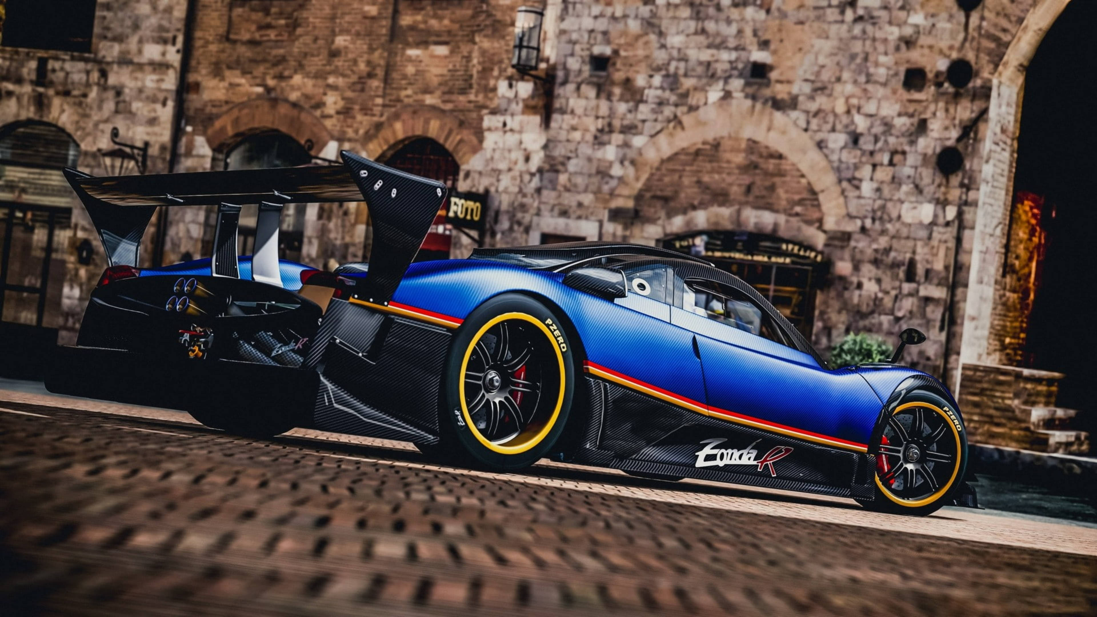 Pagani Zonda R 古石建築前 壁紙 — 一輛引人注目的藍色Pagani Zonda R超跑，配備黃色輪圈，停泊在歷史石建築前的鵝卵石路上。