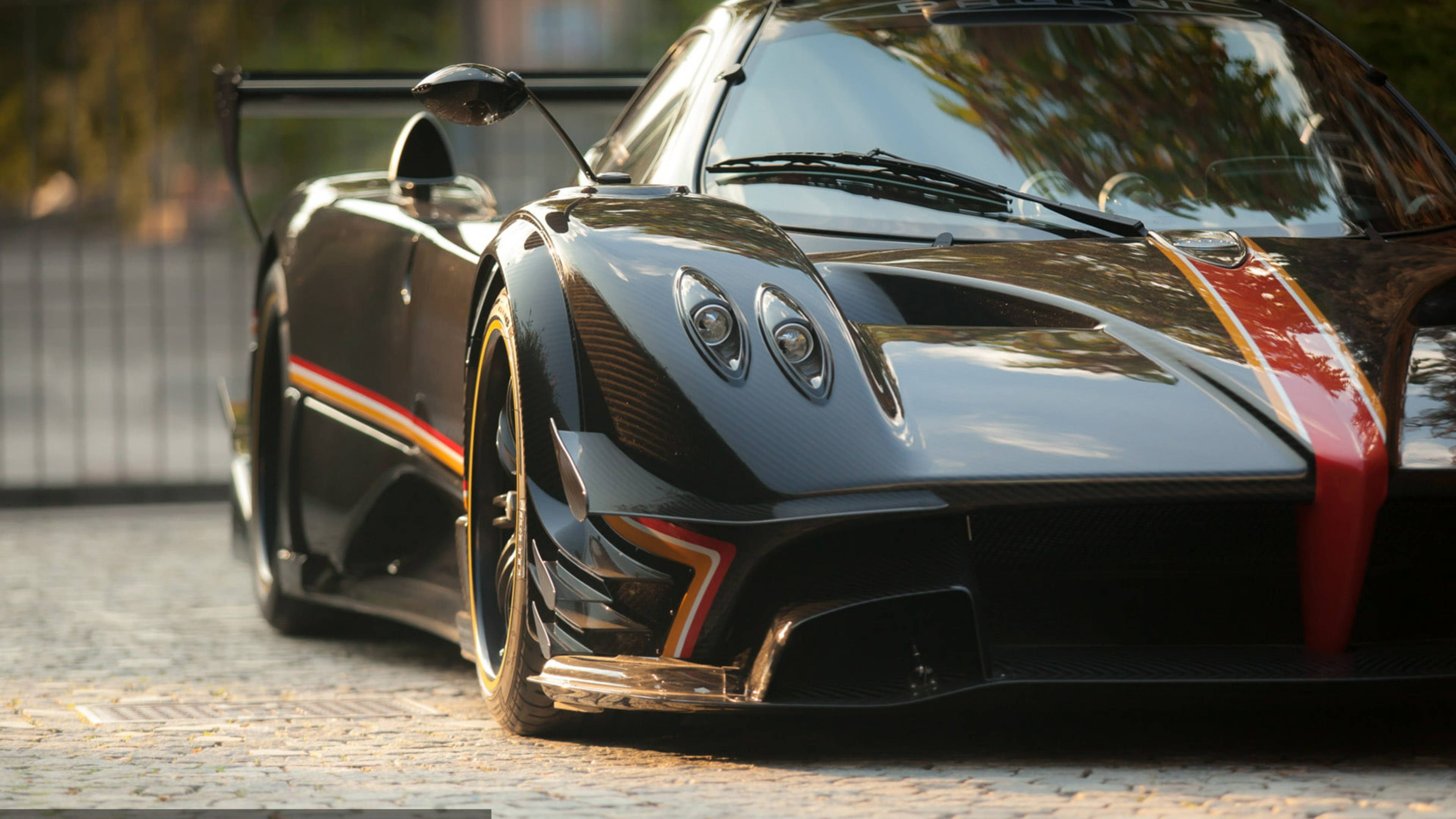 Pagani Zonda R碳纖維版 壁紙 — 一輛時尚的黑色帕加尼Huayra跑車，帶有紅色和金色點綴，停在黃金時段的鵝卵石街道上。