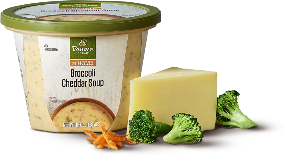 Panera 布魯西爾起司湯包裝 壁紙 — 一個Panera Bread的西蘭花切達湯容器放在一個黑暗的表面上，旁邊有一塊切達芝士和新鮮的西蘭花小朵。