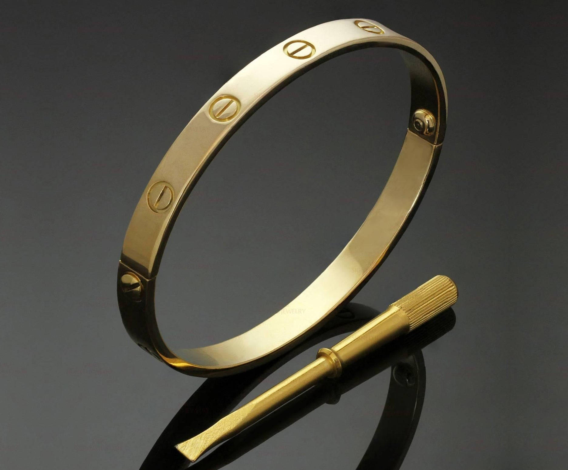 堅固卡地亞金手鐲 壁紙 — 一枚拋光金色Cartier love手鐲，帶有標誌性螺絲圖案，旁邊放著相配的金色螺絲刀，置於深色反光表面上。