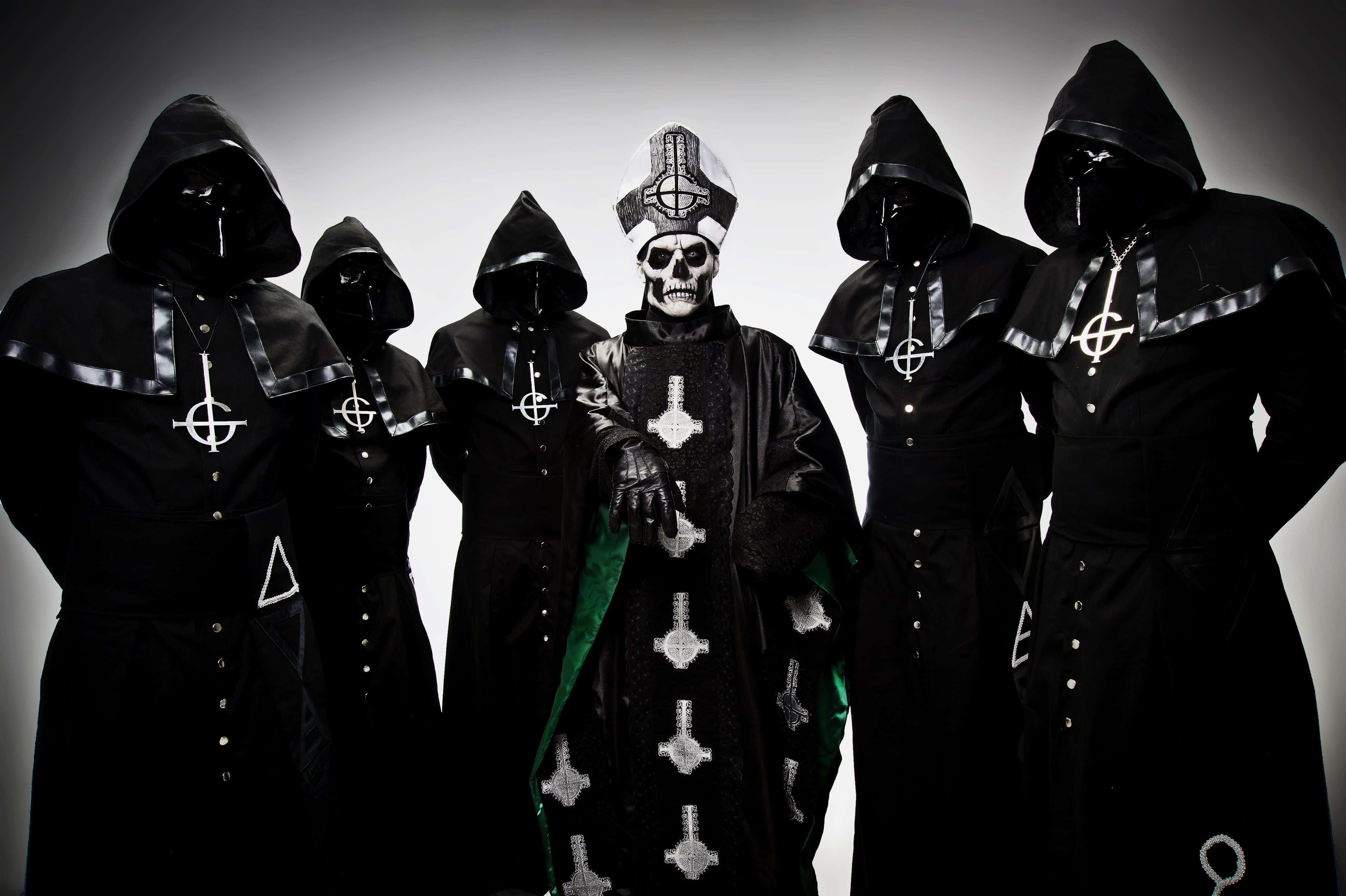 Papa Nihil被Ghost樂隊成員環繞 壁紙 — 一個身穿華麗黑色長袍、帶有銀色十字架的骷髏人物站在舞台中央，被身穿相配深色服裝的戴兜帽人物包圍，背景是鮮明的漸變色。