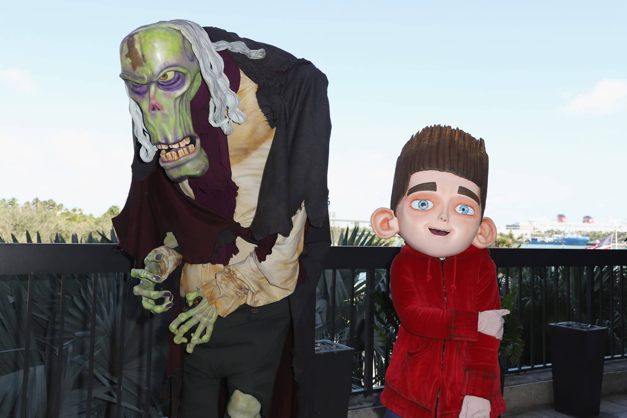 殭屍法官與諾曼 ParaNorman 壁紙 — 一個綠色皮膚的喪屍服裝和一個卡通男孩剪影並排站在陽台上，背景是晴朗的天空。