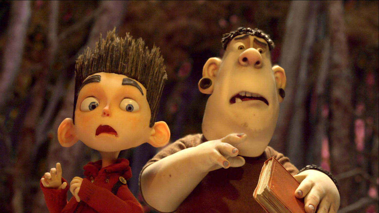 驚恐的阿爾文與諾曼 ParaNorman 壁紙 — 兩個表情誇張的動畫角色站在昏暗的森林中，其中一個拿著書本急切地指向某處。