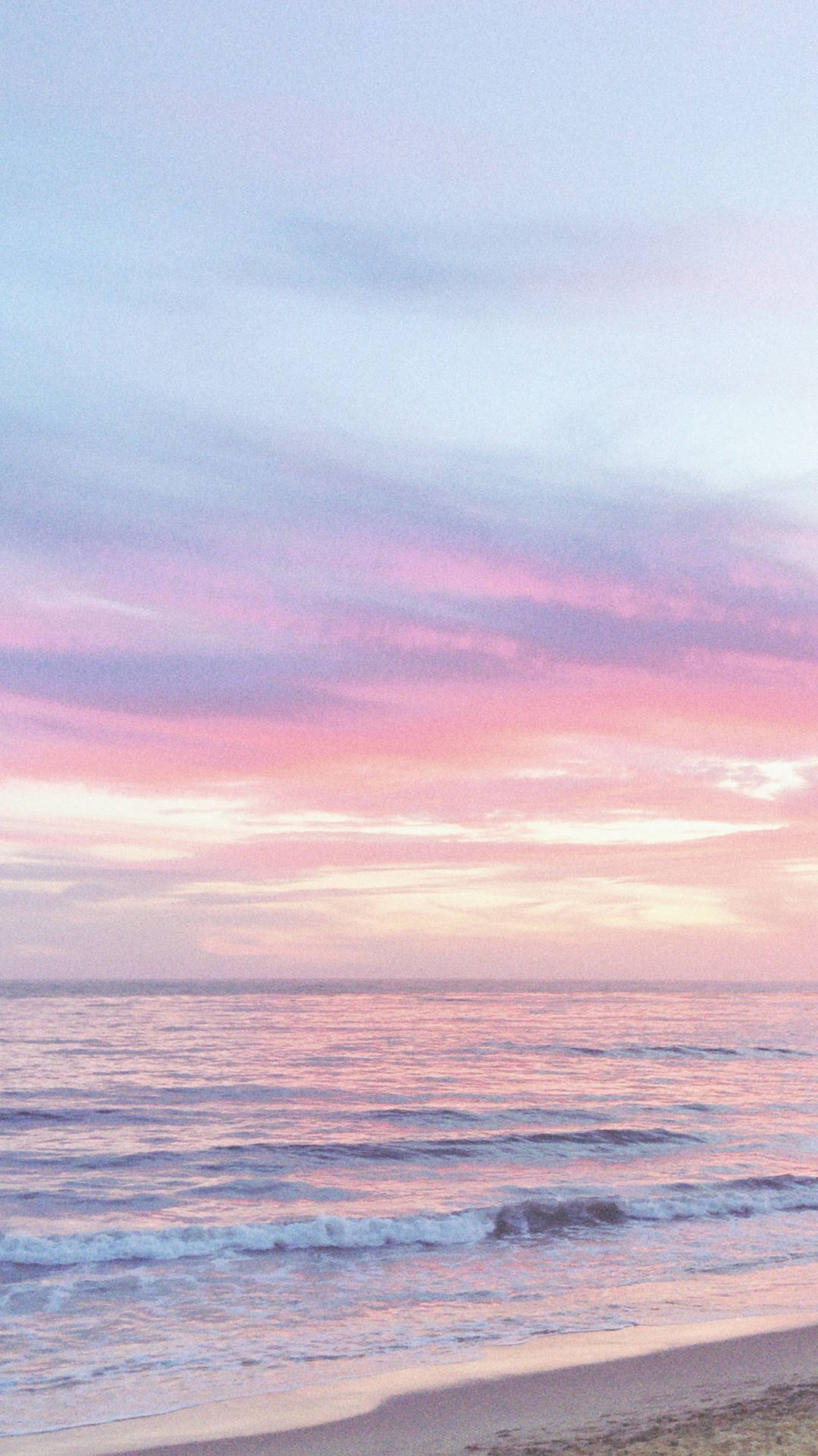 粉紅色和薰衣草色的日落，映照在沙灘上平靜的海浪上。
