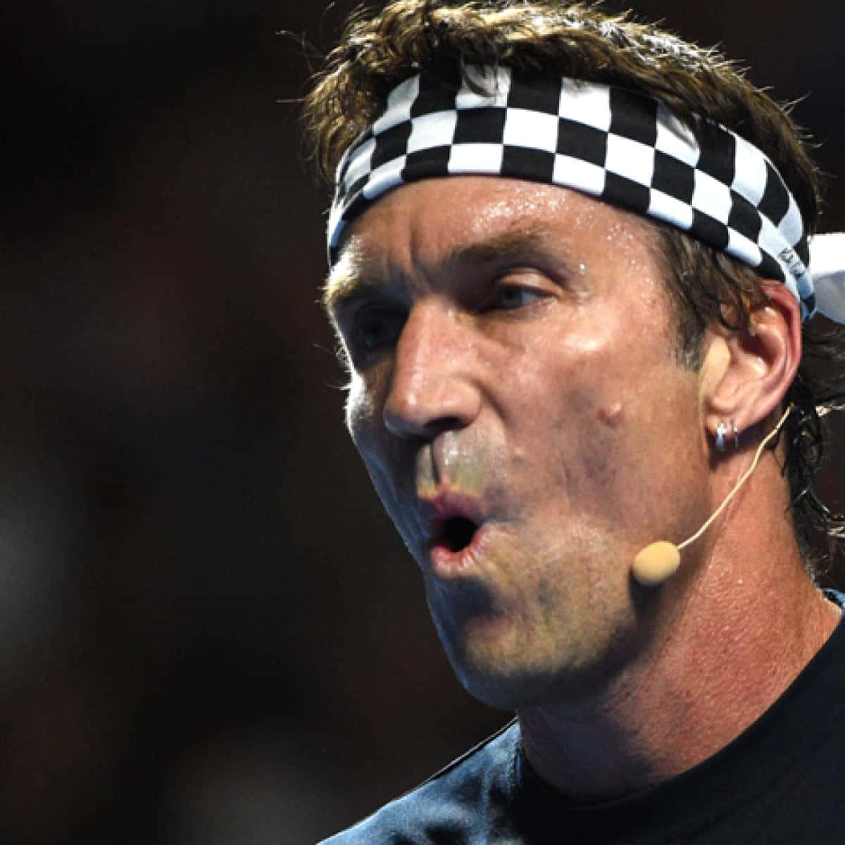 Pat Cash 戴黑白髮帶照片 壁紙 — 一名汗流浹背的男子近照，戴著黑白格仔頭帶和咪高峰耳機。