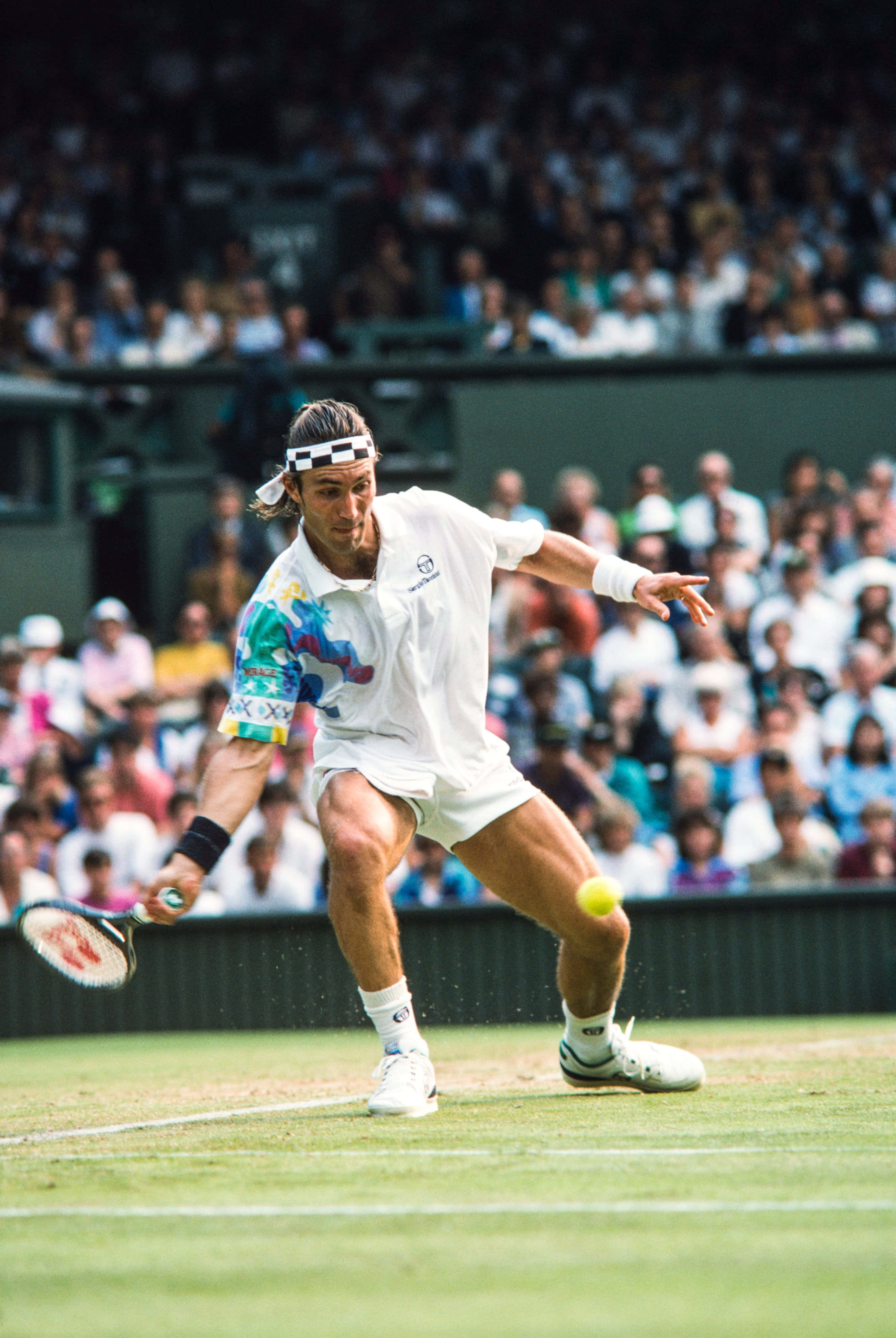 Pat Cash 經典肖像風桌面壁紙 壁紙 — 一名身穿白色裝備的男網球手在草地場上向前猛衝，用球拍擊打黃色球，觀眾在看台上觀看。