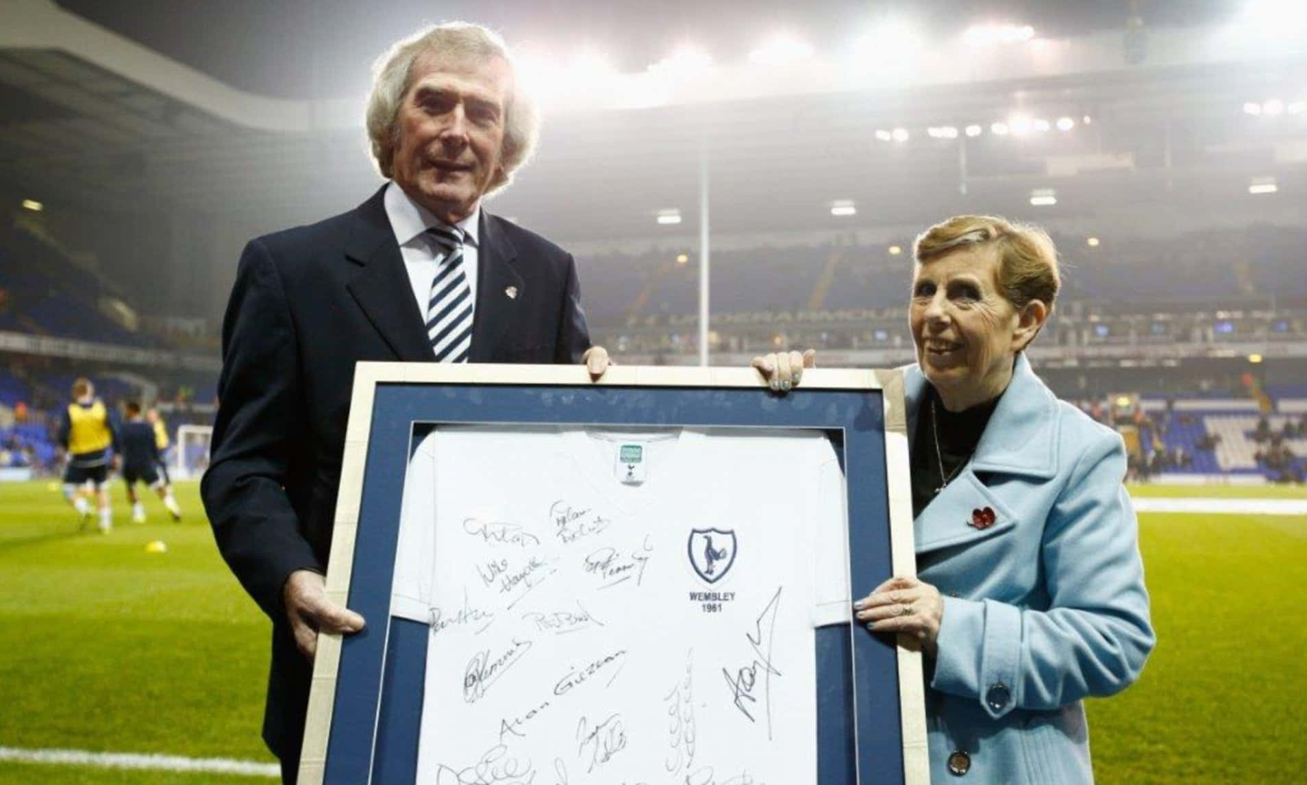 Pat Jennings 於 2015 年 Hotspur Hero 頒獎典禮 壁紙 — 兩個微笑嘅人喺球場上，喺明亮燈光下，舉起一個裝裱好嘅簽名足球波衫。
