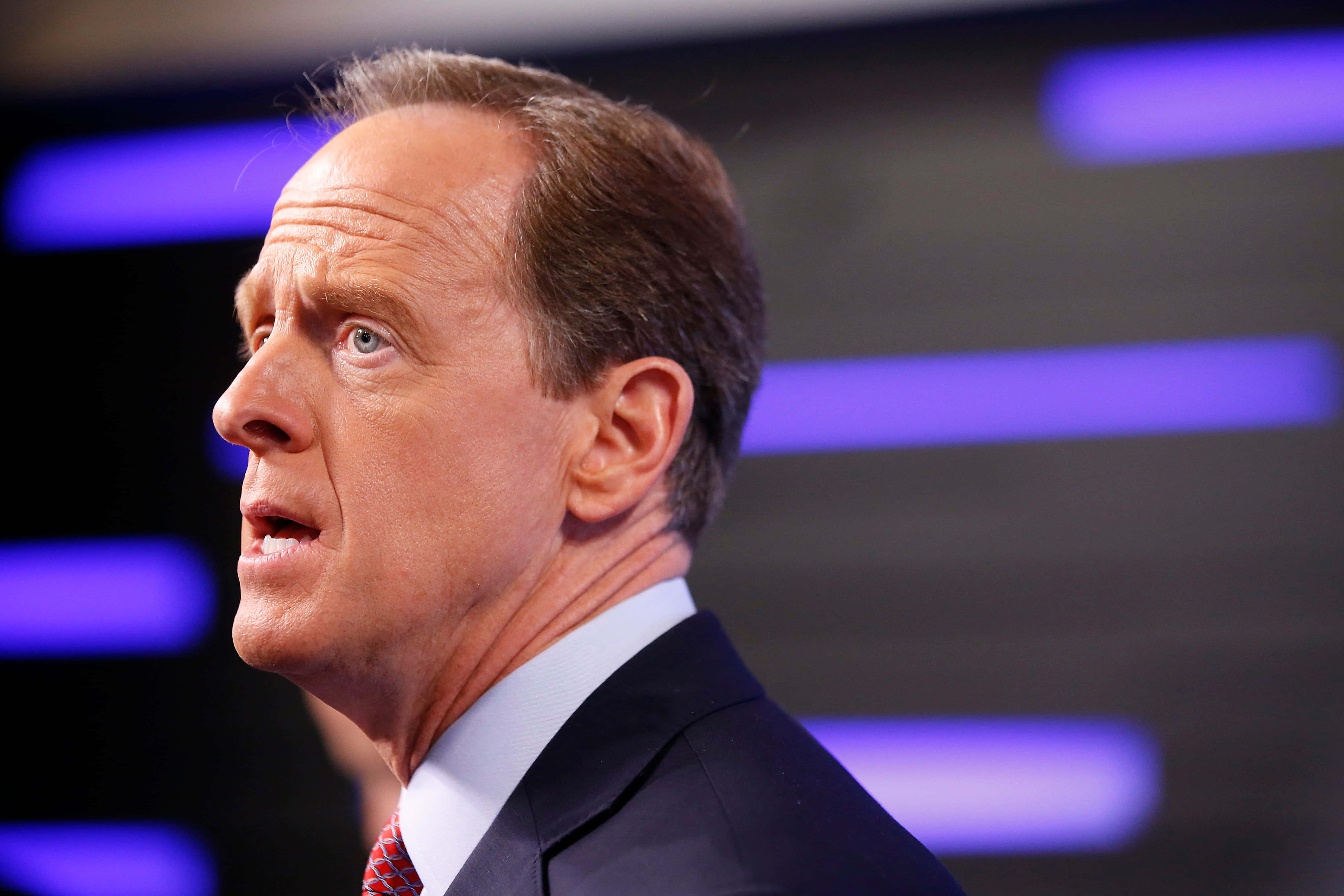 Pat Toomey向左凝視 壁紙 — 一名身穿西裝的男子在模糊的紫色燈光背景下激烈地說話。