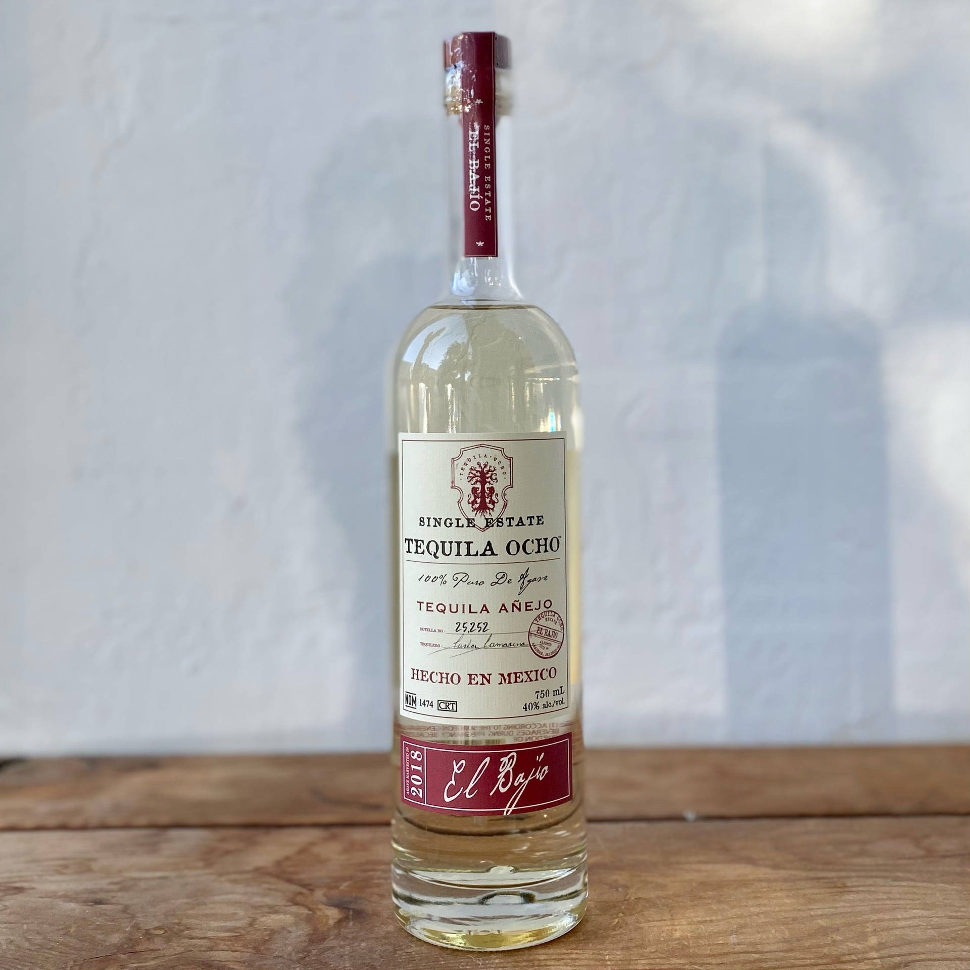 一個Tequila Ocho Añejo酒瓶放在木桌上，背景是白色牆壁。