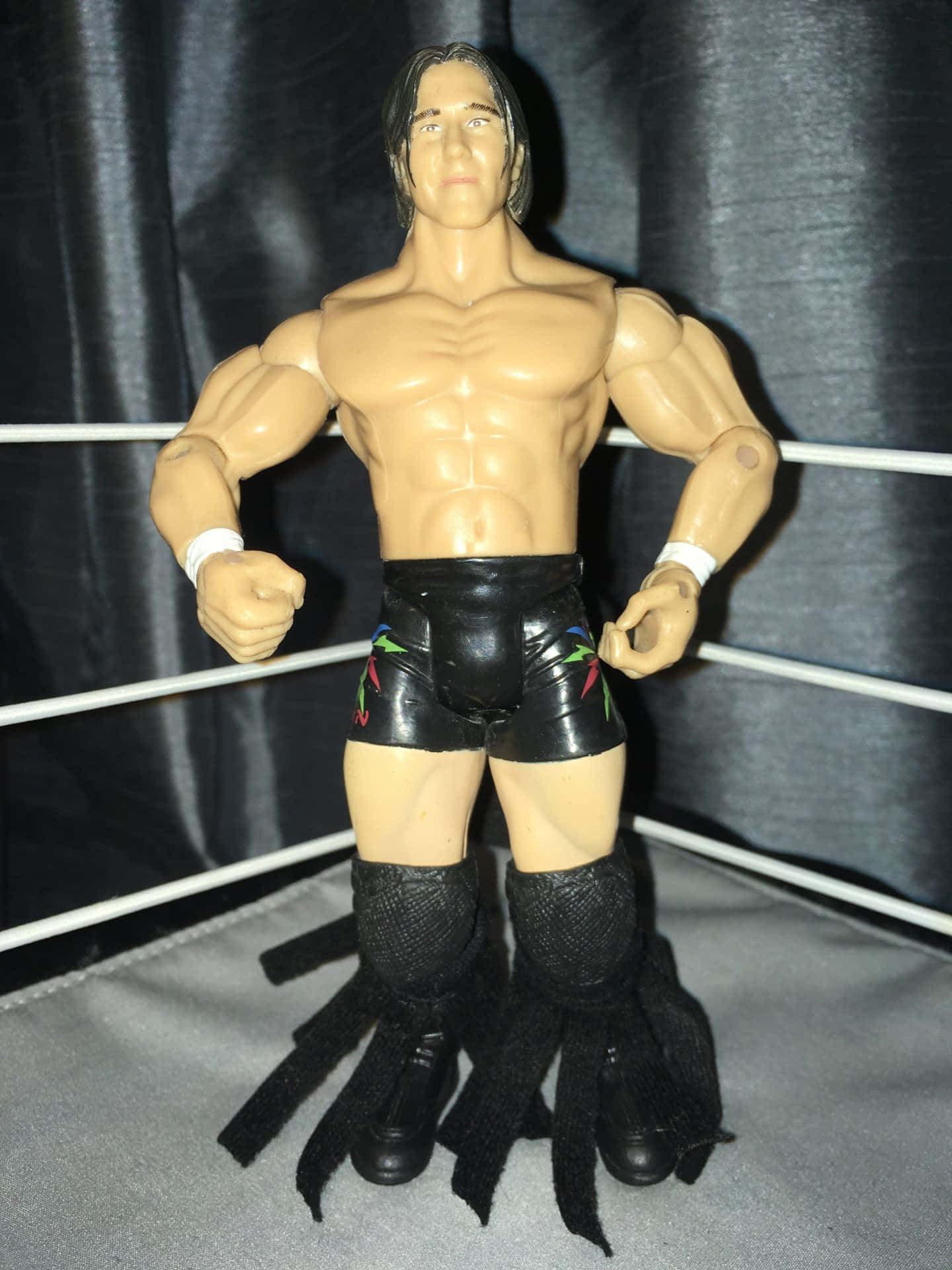 WWE摔角手動作人偶在摔角擂台上擺姿勢，穿著黑色緊身褲和護膝。