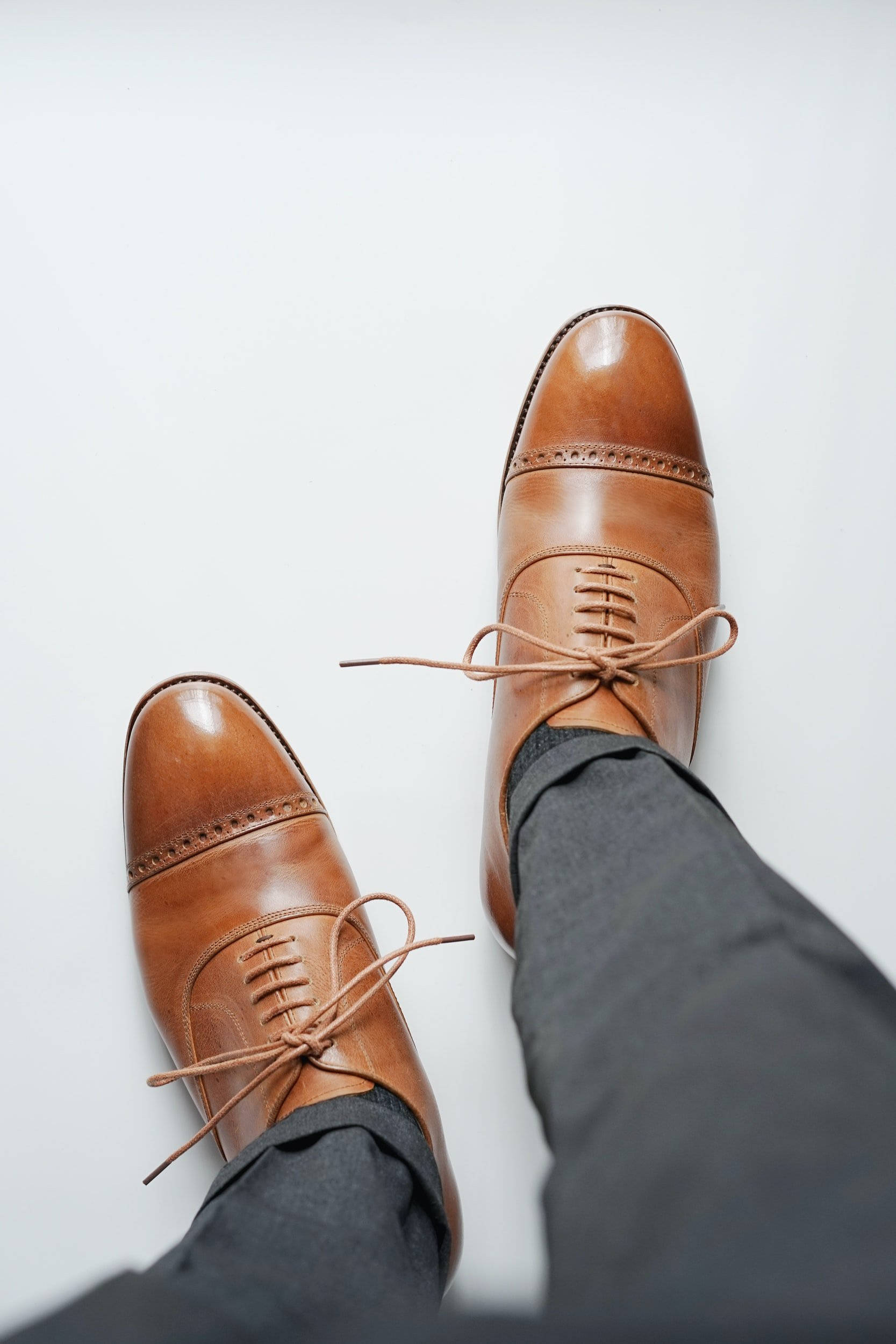 Paul Stuart 優雅棕色禮服鞋 壁紙 — 從上方俯瞰拋光棕色皮革 cap-toe 正裝鞋，鞋帶未繫，置於純白背景上。