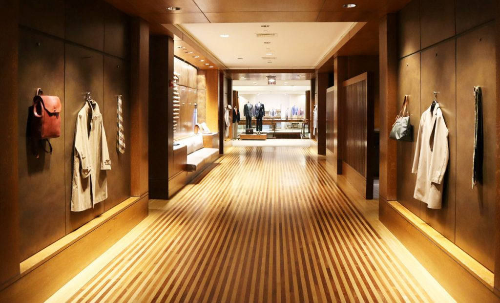 一個木地板的服裝店走廊，展示牆上掛著外套和手袋。