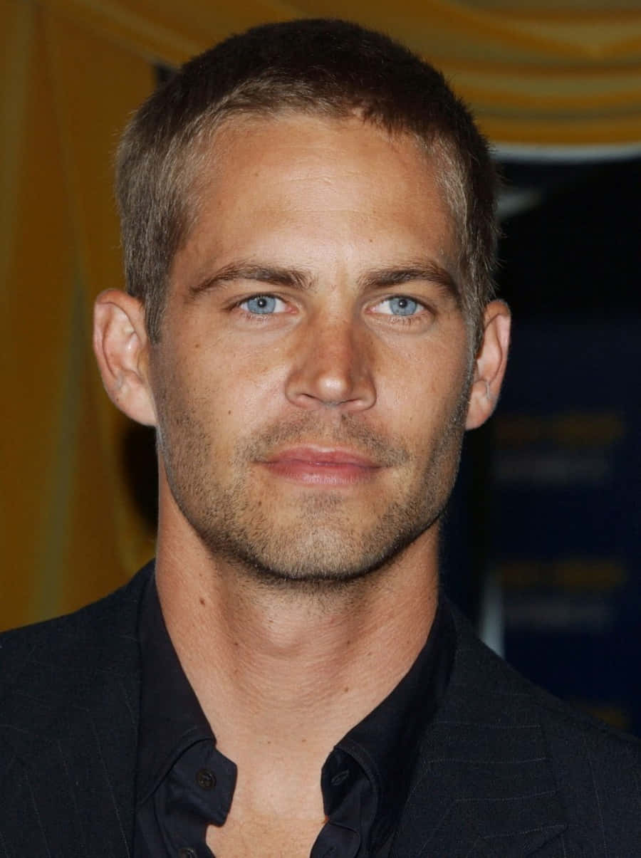 Paul Walker 桌布 壁紙 — Paul Walker 嘅近距離肖像，藍眼睛、鬚根，身穿深色西裝，背景模糊黃藍色。