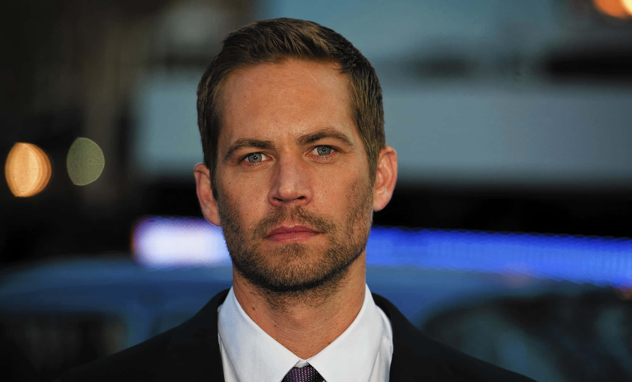 保羅·獲加 桌布 壁紙 — Paul Walker 身穿深色西裝和領帶的 close-up 肖像，背景是模糊的城市夜景和散景燈光。
