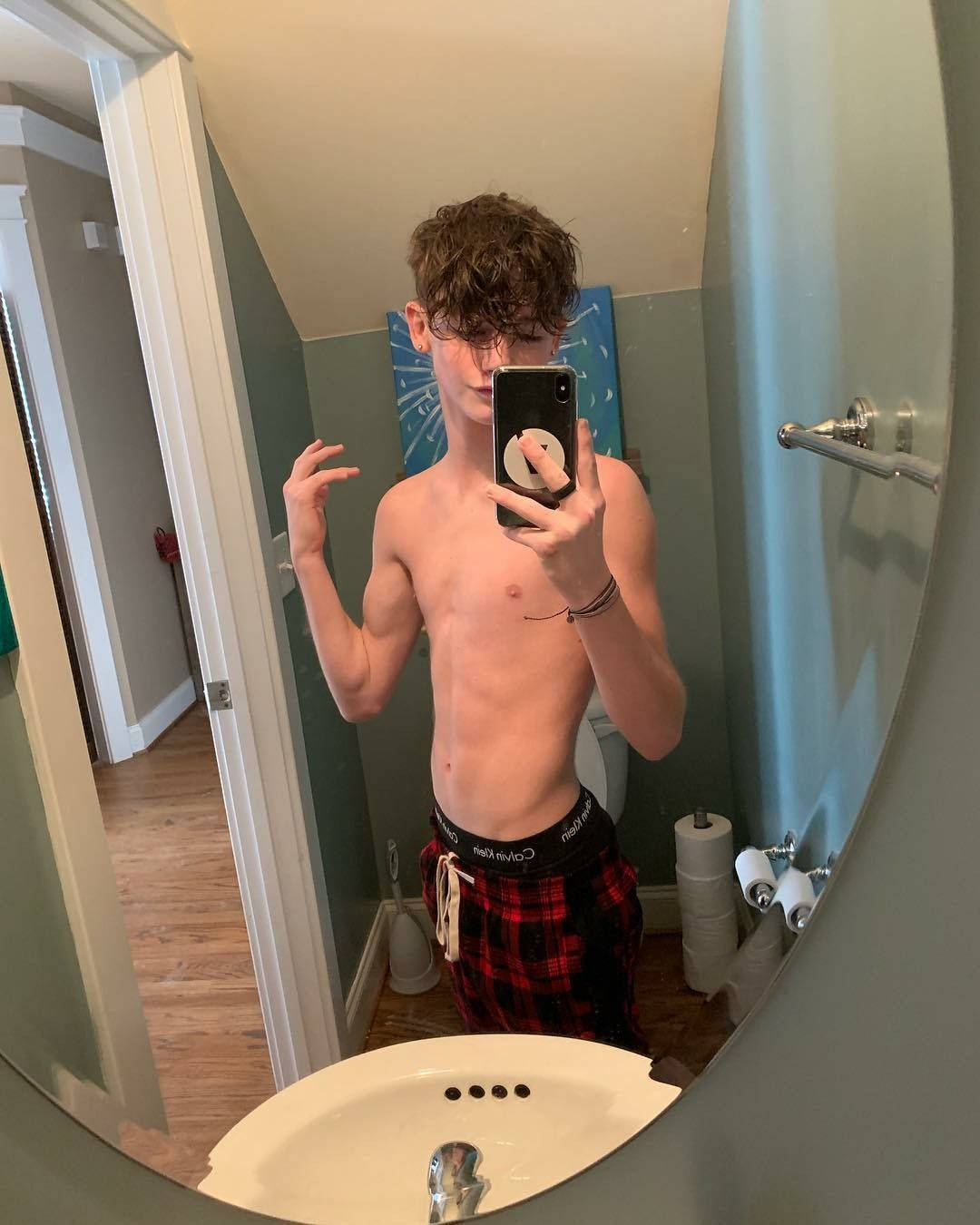 Payton Moormeier 鏡前自拍 壁紙 — 一個赤膊、捲髮的年輕男子在浴室穿著格仔短褲對著鏡子自拍。