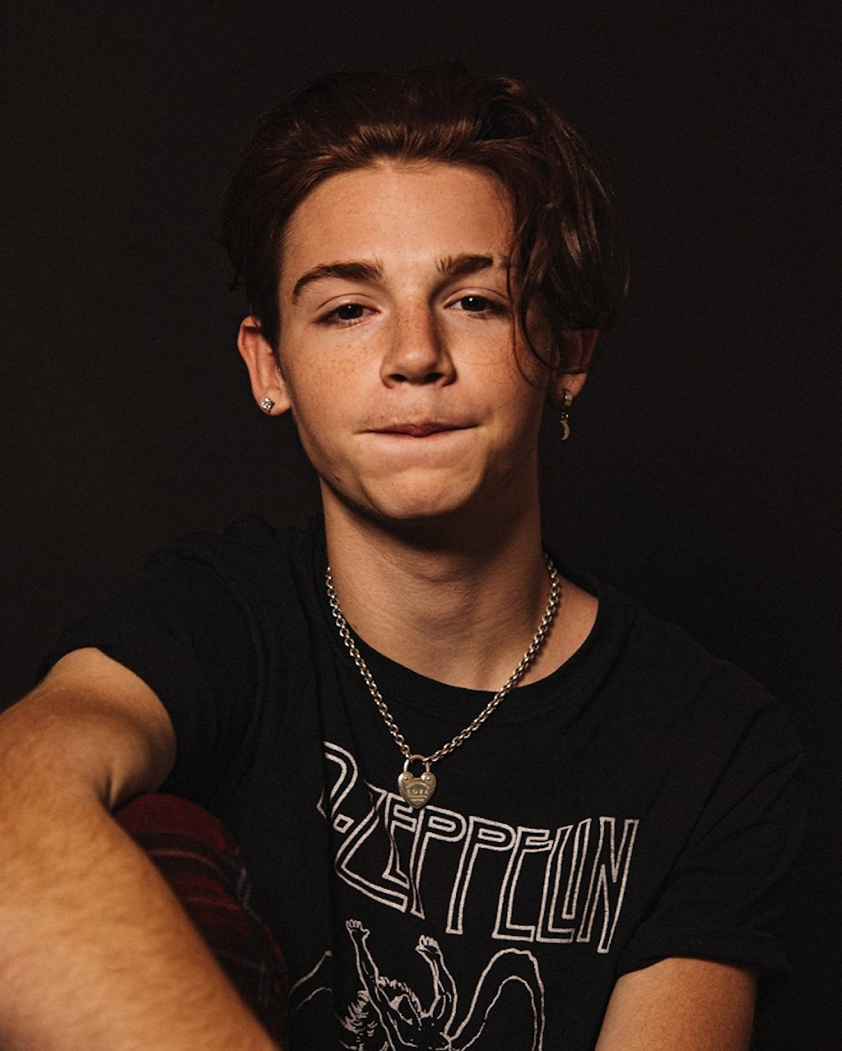Payton Moormeier 咬唇特寫 壁紙 — 一位棕色頭髮、有雀斑的年輕男子，身穿黑色Led Zeppelin T恤和銀色首飾，背景為深色。