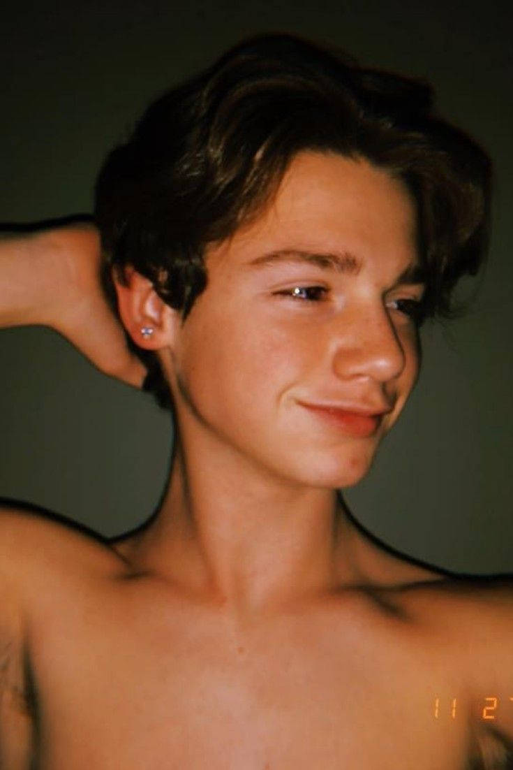 Payton Moormeier 面部肖像 壁紙 — 一名冇著衫嘅深色頭髮年輕男子，帶住微妙嘅笑容，喺柔和綠色牆前面用手撥頭髮。