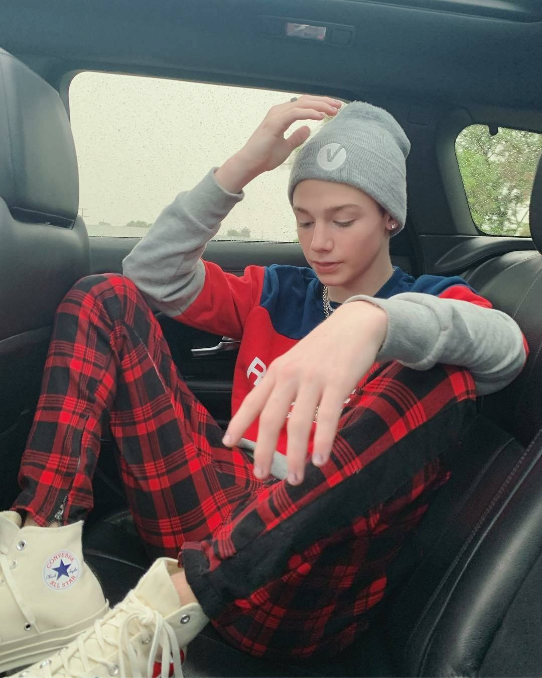 Payton Moormeier 戴著毛線帽 壁紙 — 一個戴灰色冷帽、穿紅色格仔褲的年輕人，隨意地坐在汽車後座，手放在頭上，低頭看着。