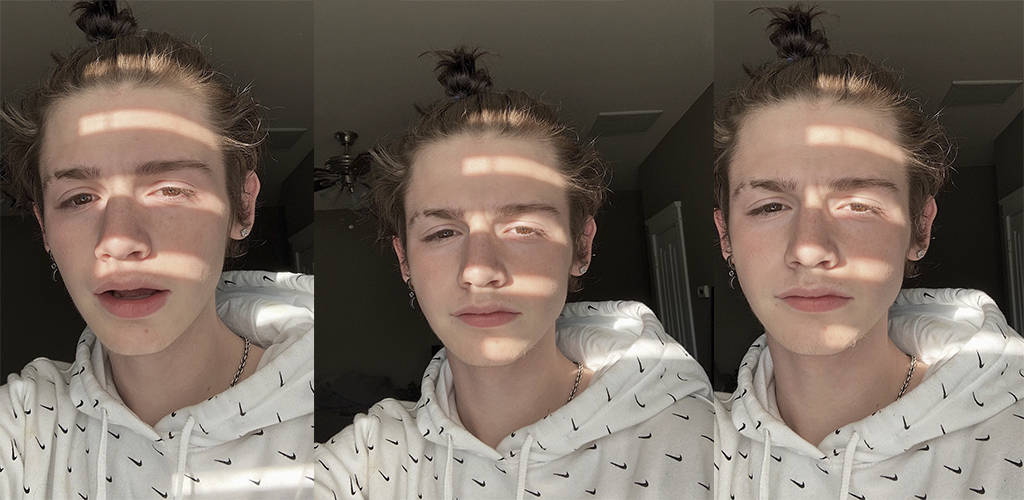 Payton Moormeier 穿白色連帽衫 壁紙 — 一位年輕人的頭髮紮成髮髻，身穿白色連帽衫，陽光在他們臉上投射出條紋陰影，形成一幅三聯自拍。